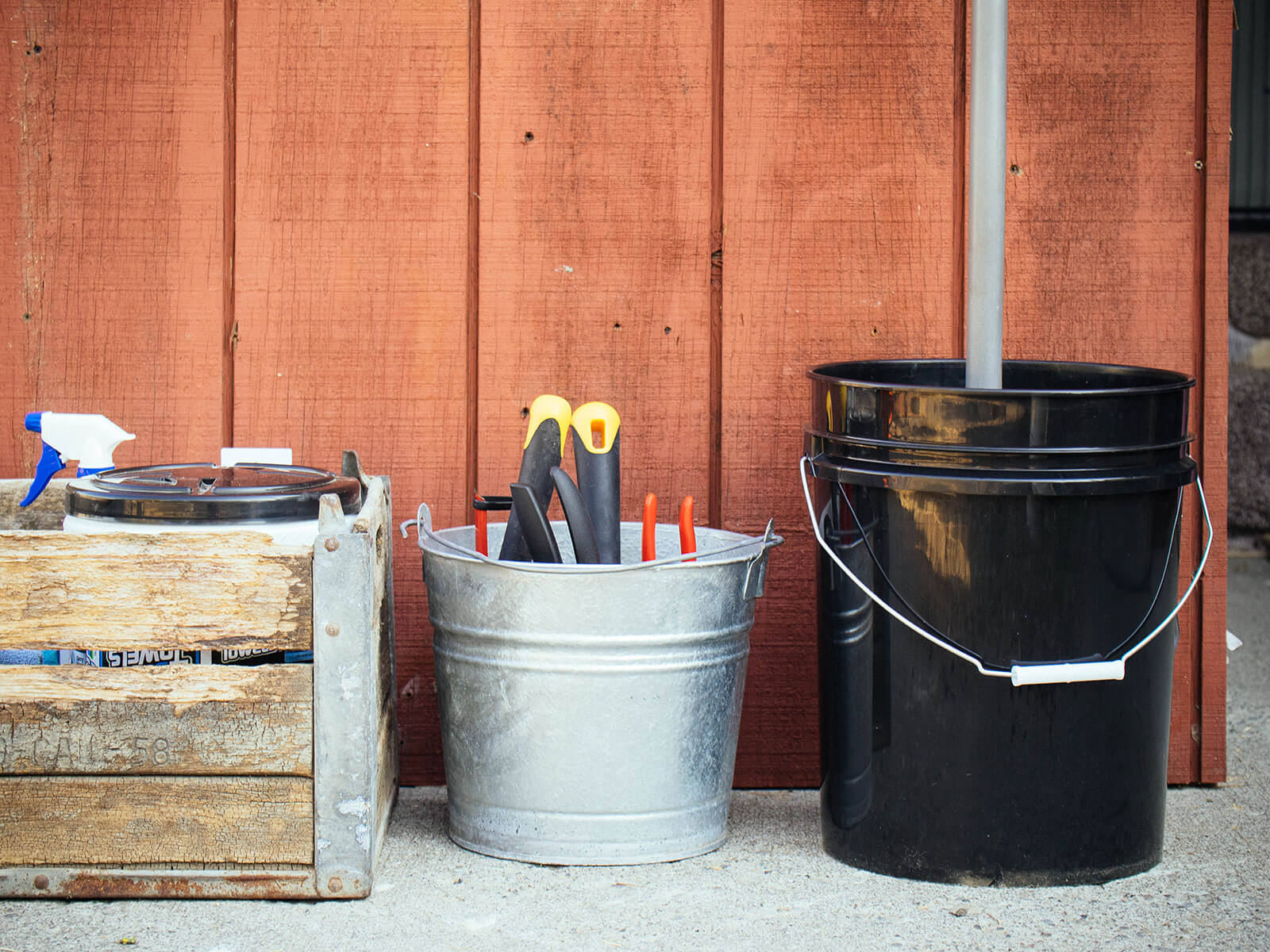 Crate of cleaning supplies and two buckets filled with tools, set against a shed wall