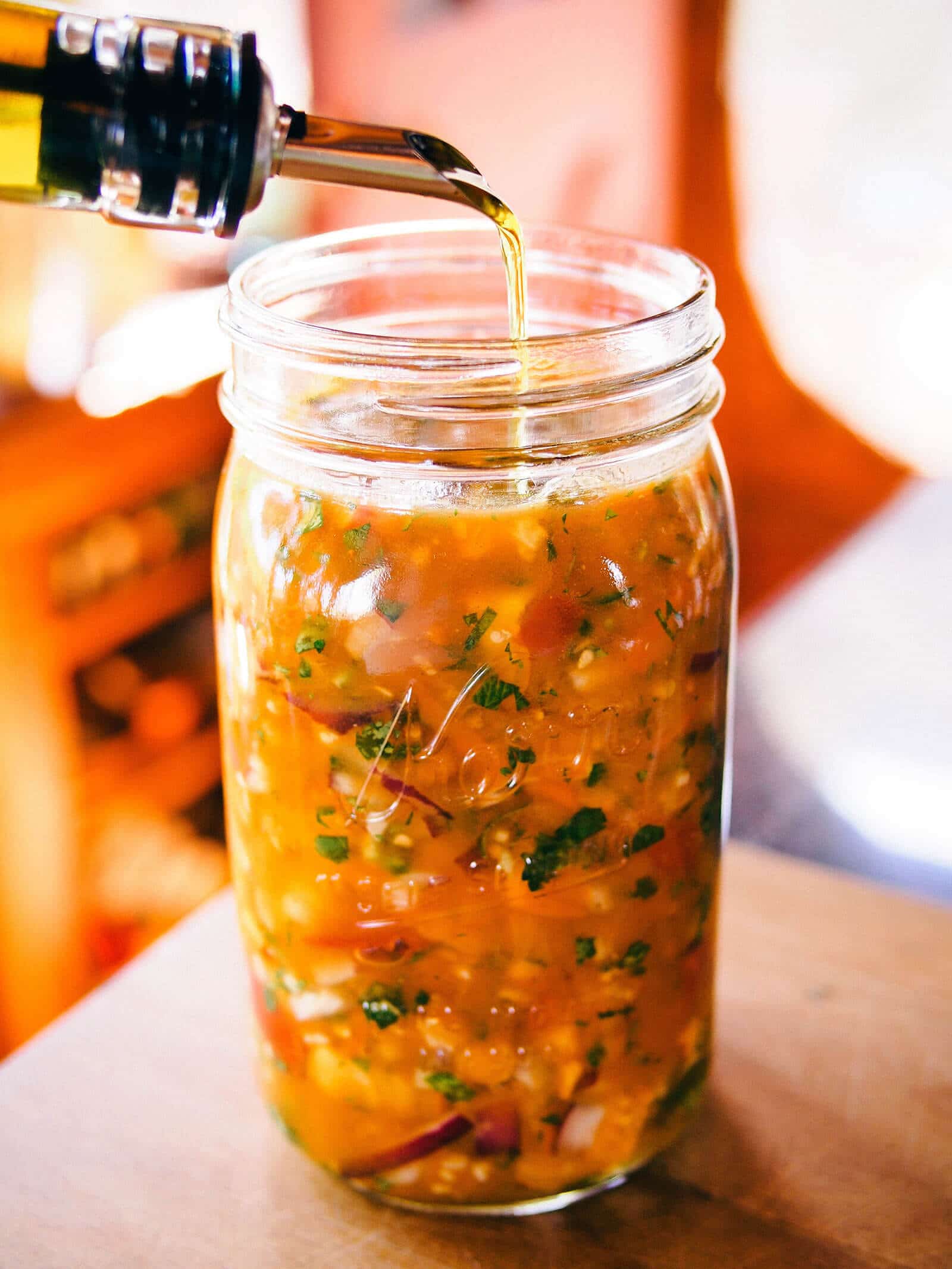 Olive oil pouring into a jar of salsa