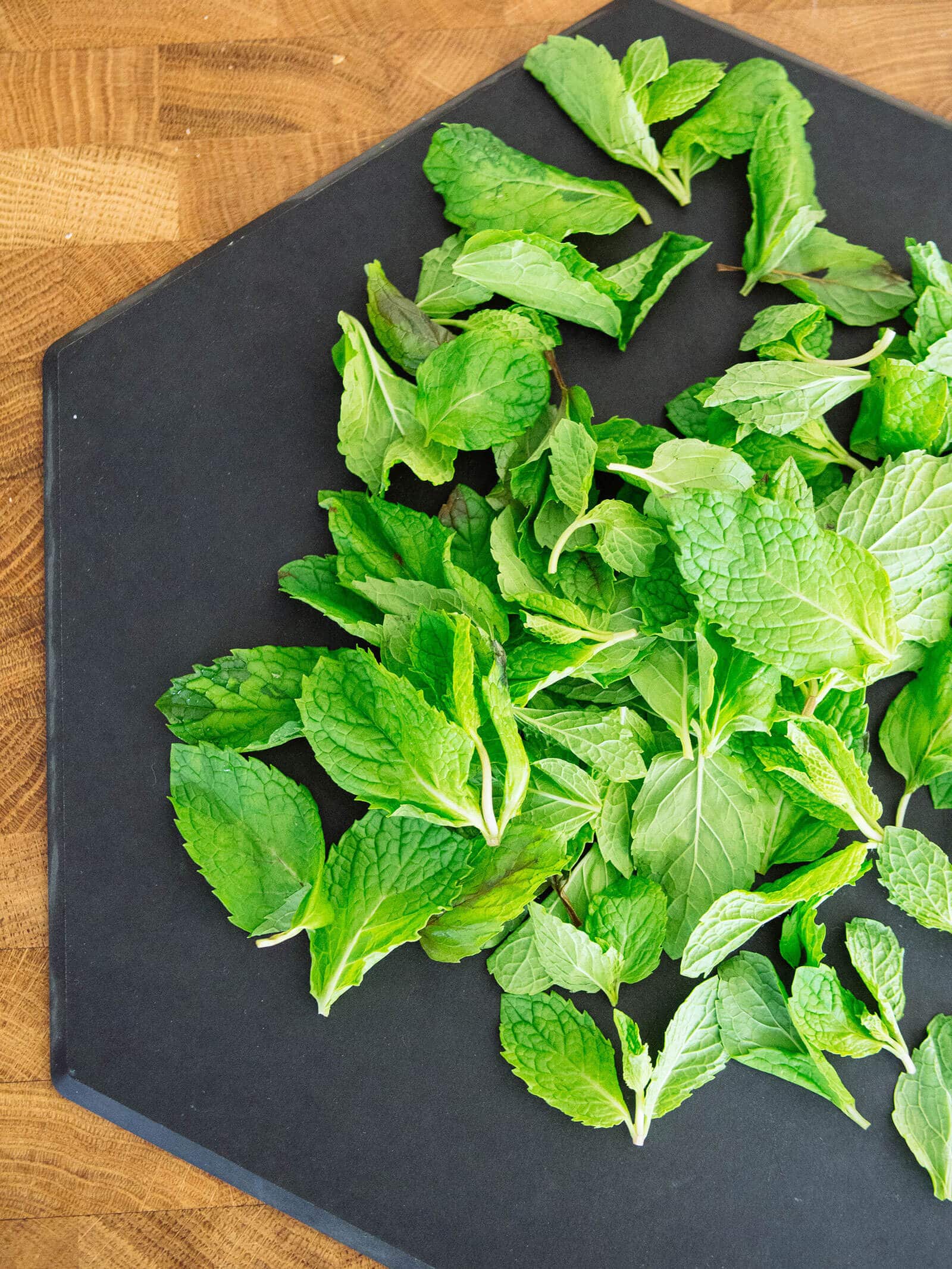 Freshly picked mint leaves spread out on a black cutting board