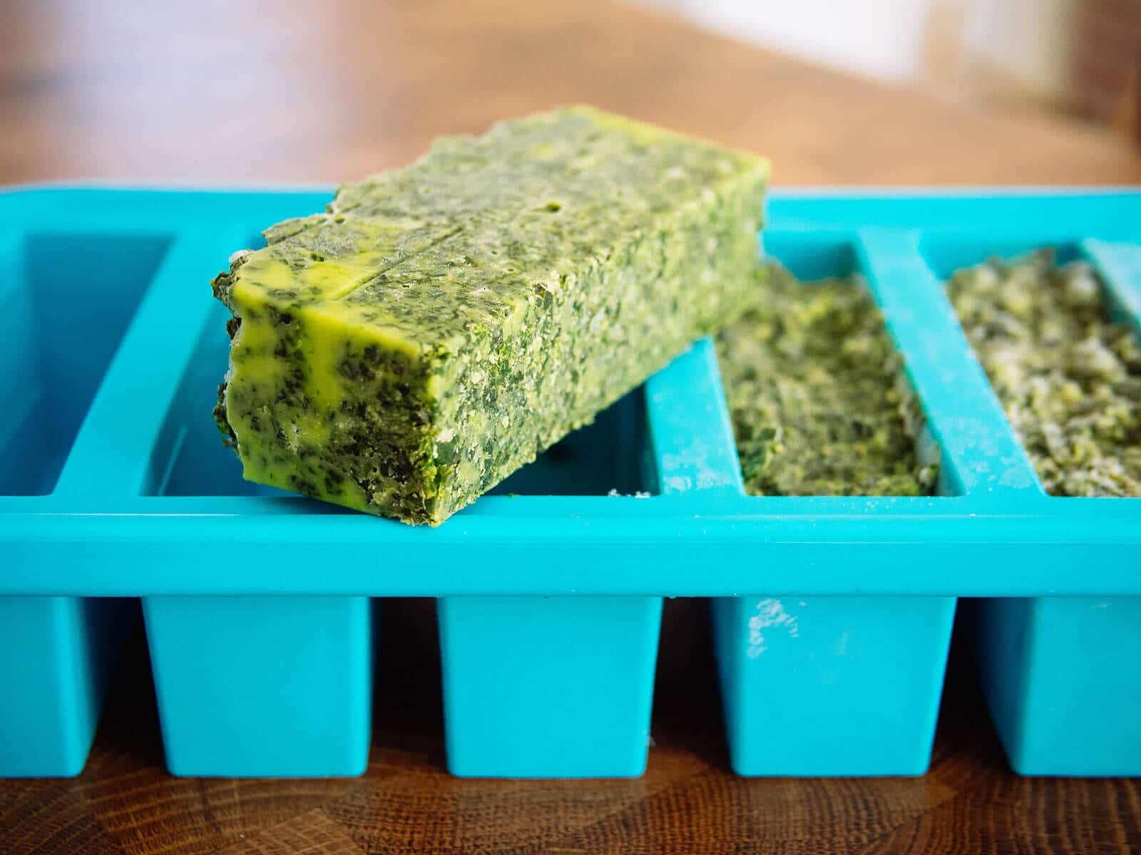 A frozen bar of basil pesto sitting on top of a blue ice cube tray