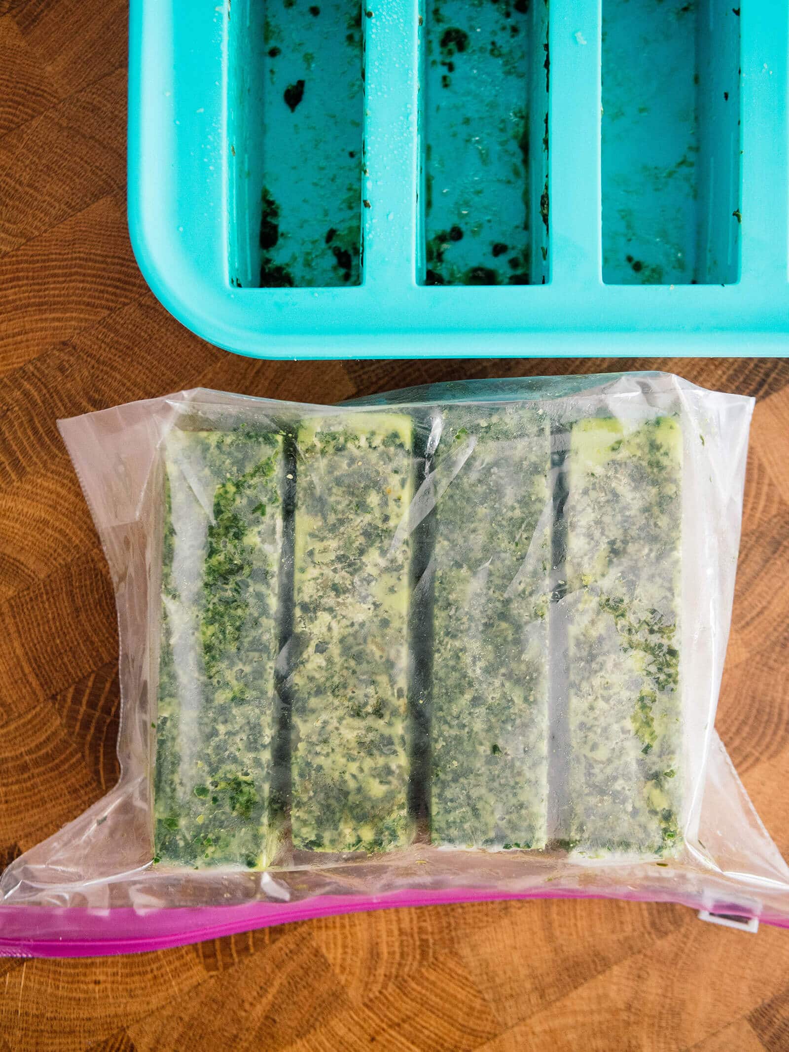 Frozen pesto bars stored in a freezer bag next to an empty ice cube tray