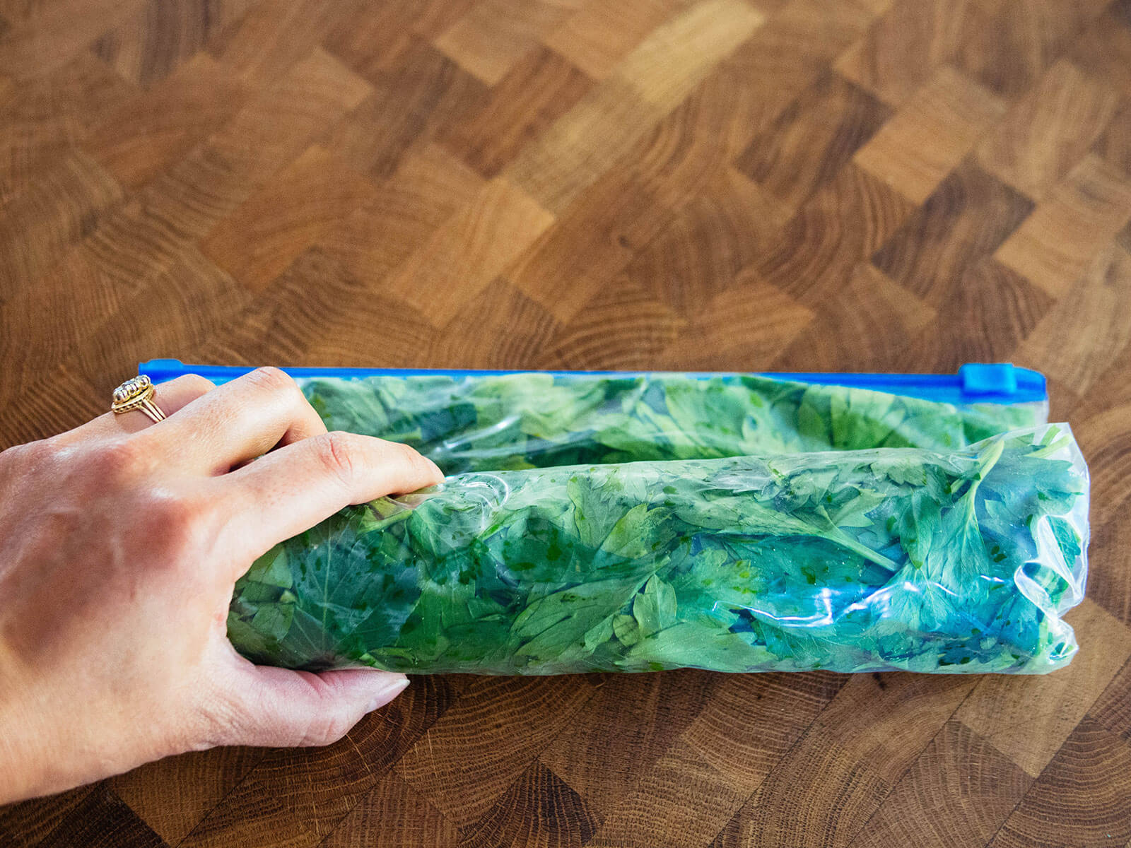 Hand rolling up a freezer bag full of parsley to form a log