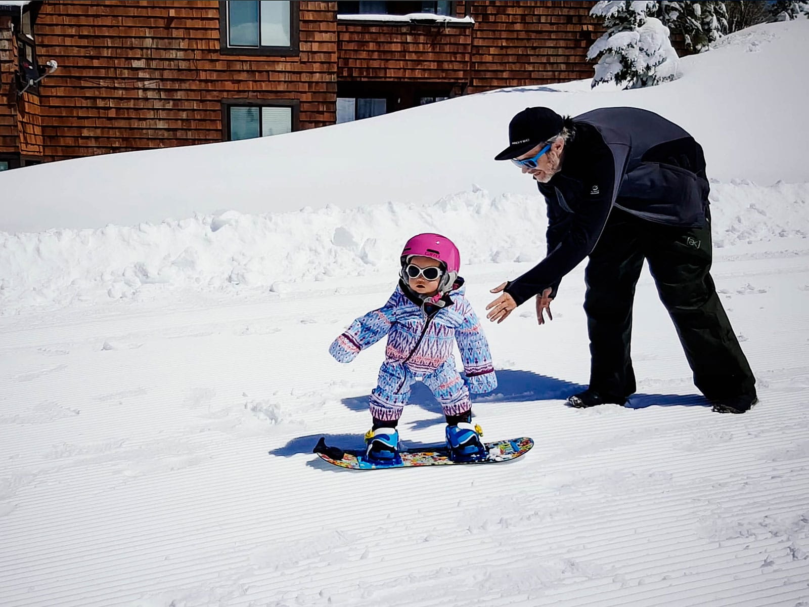 A parent teaching a 1-year-old how to snowboard