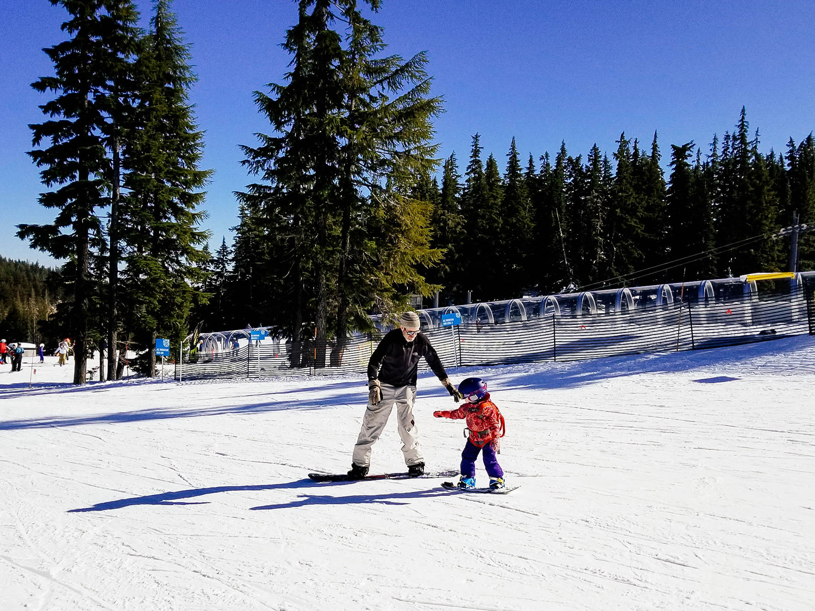 A parent teaching a 3-year-old how to snowboard at a ski resort