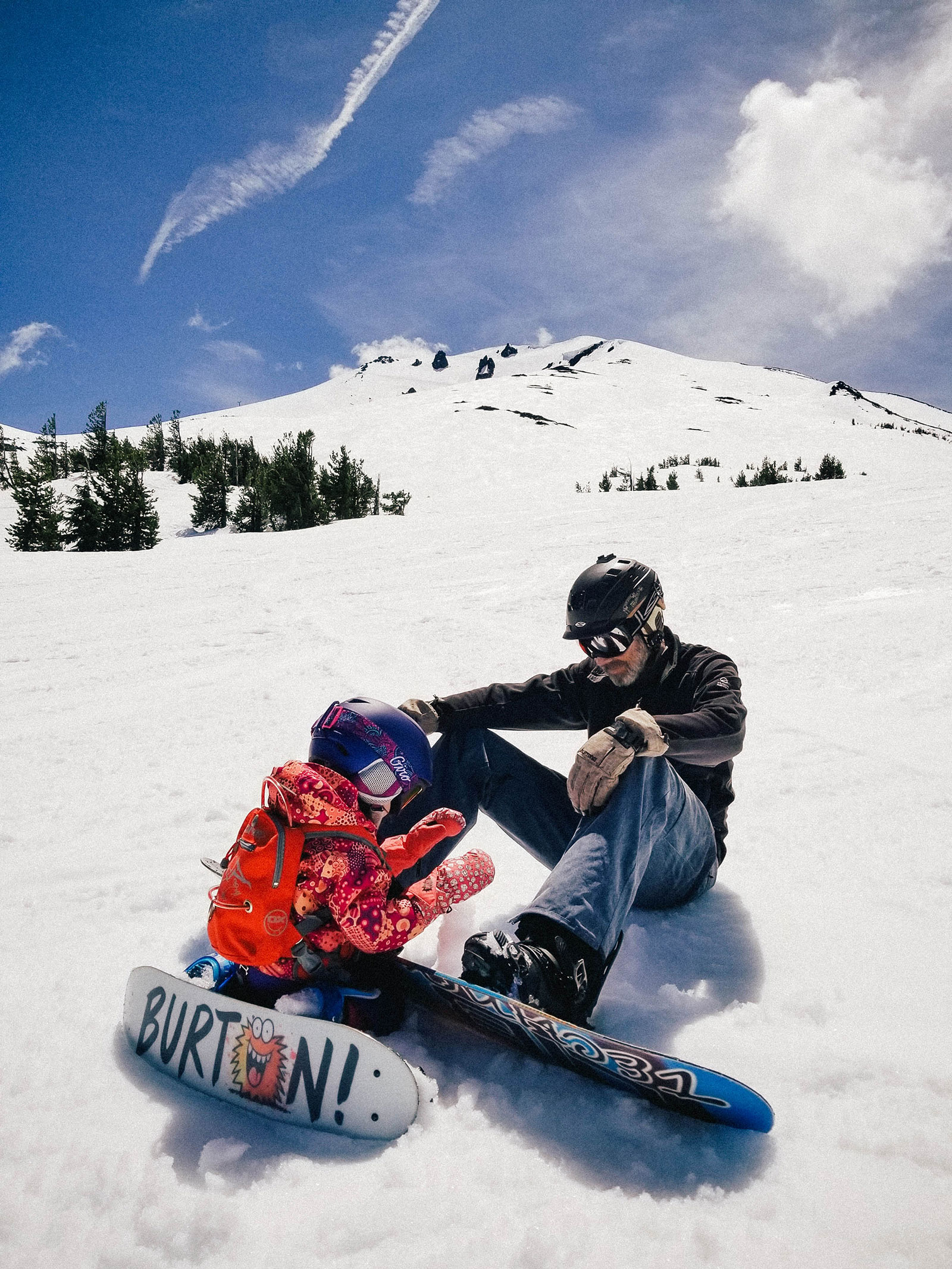 Snowboarding toddler taking a break on the mountain and building a mini snowman with Dad