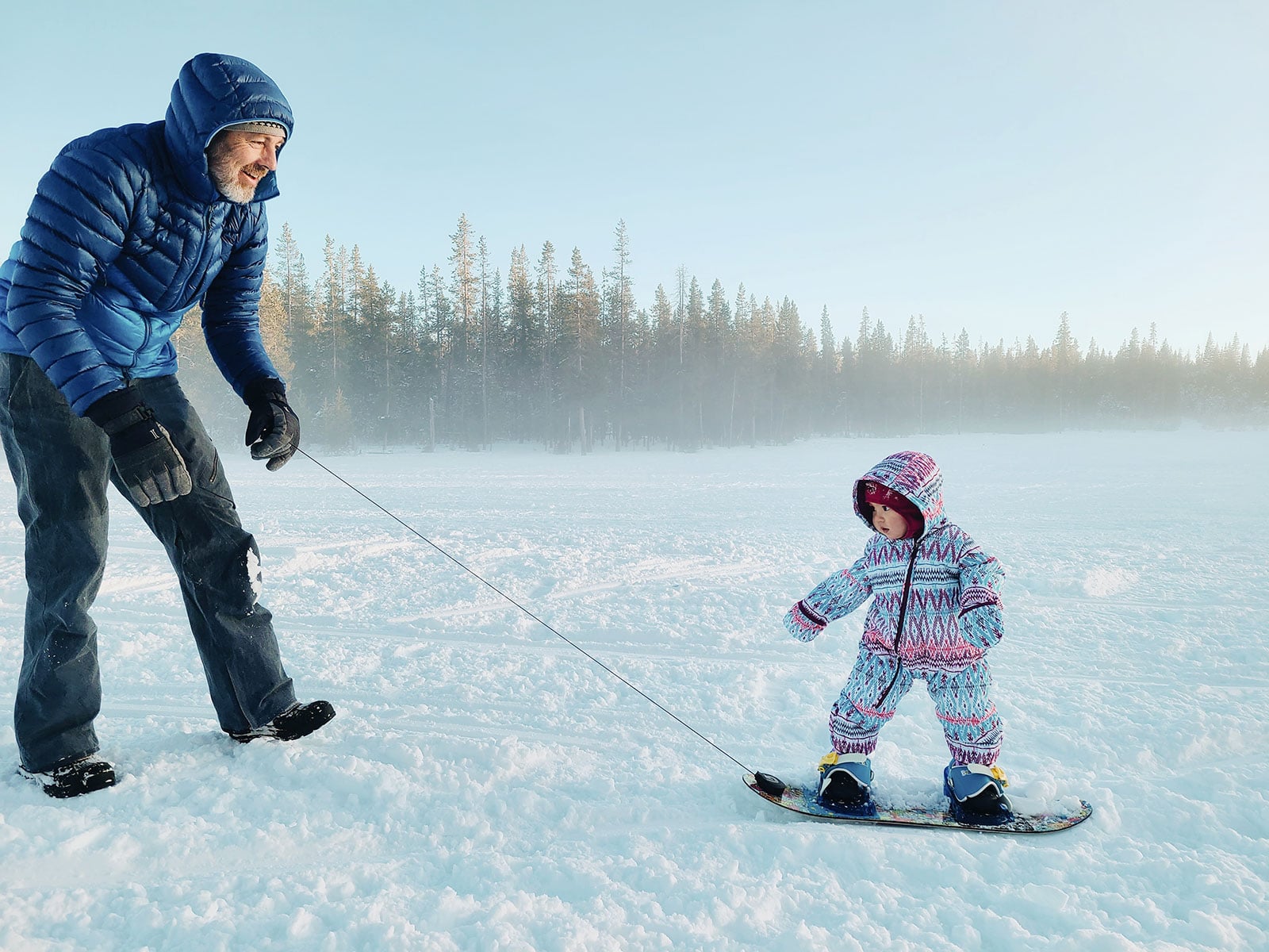 Dad using the Burton Riglet Reel to tow a 1-year-old baby around on a snowboard