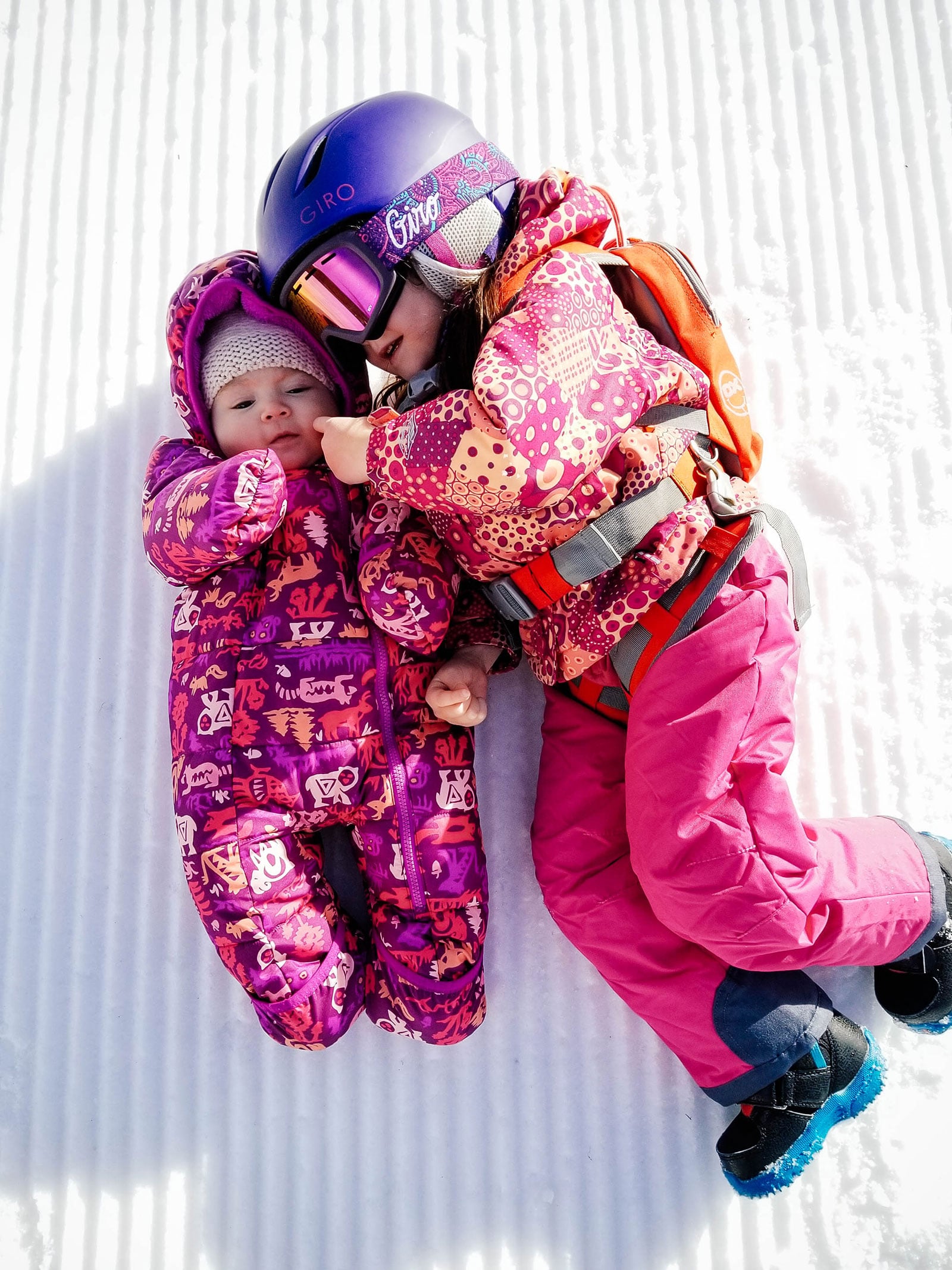 A baby and toddler lying in the snow together