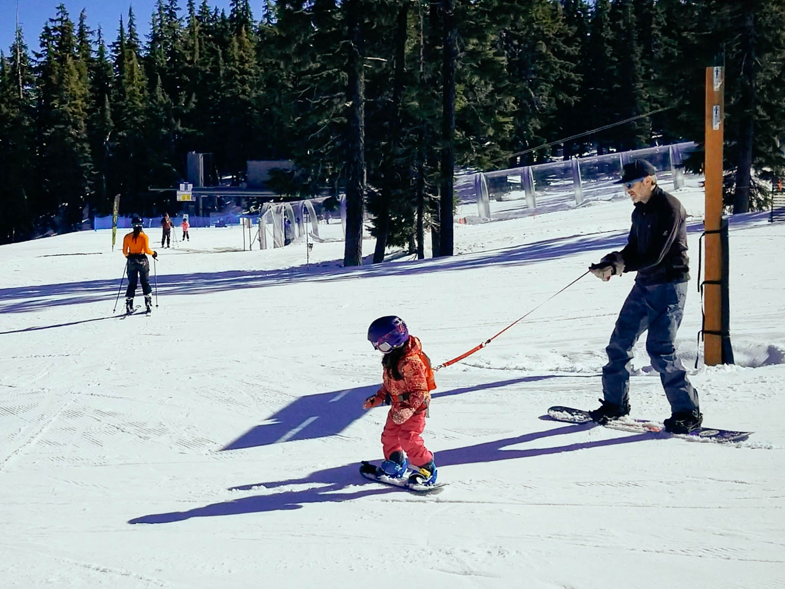 Dad using a backpack harness to guide his toddler down the mountain on a snowboard