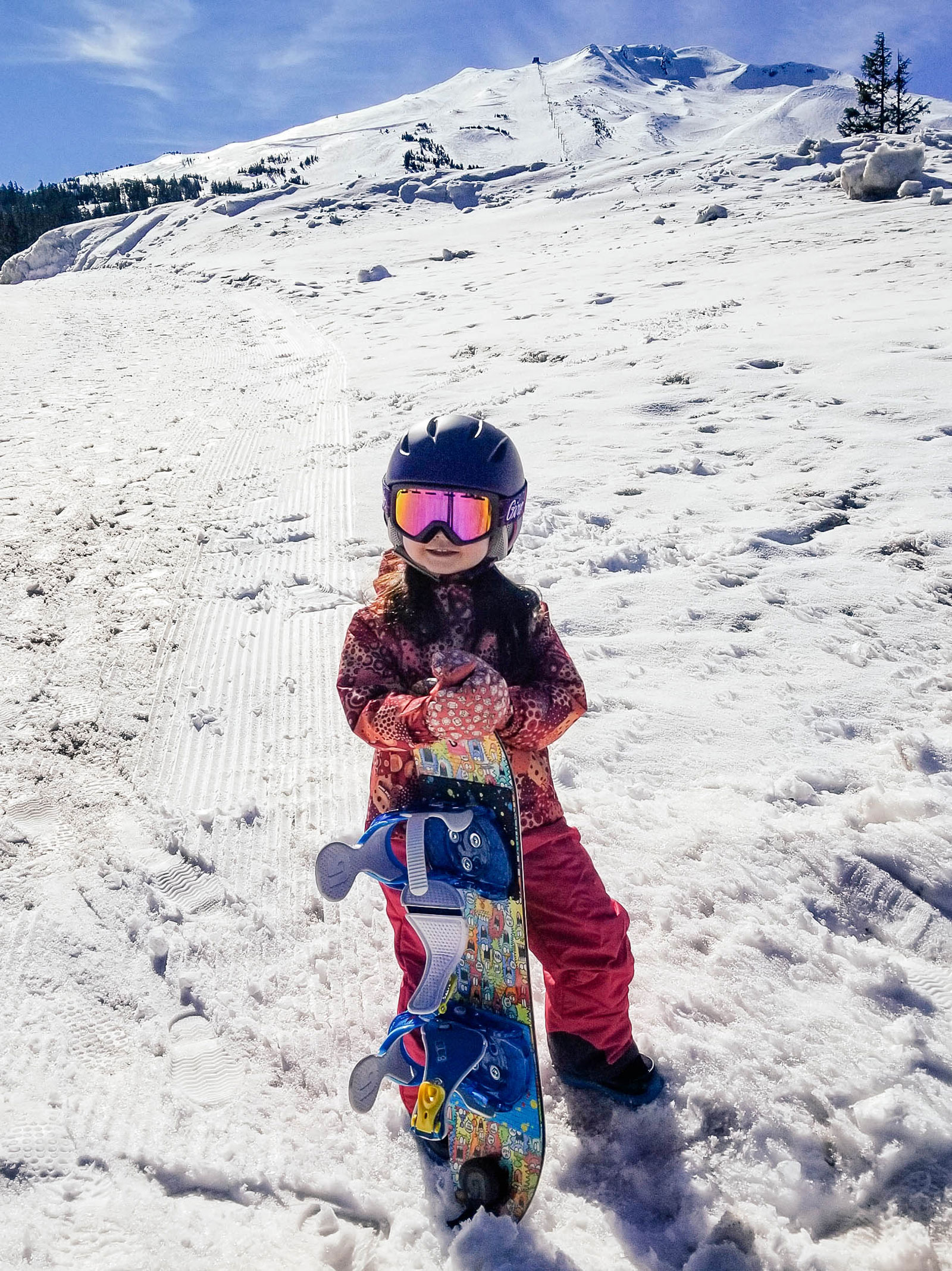 A 3-year-old toddler holding her snowboard and feeling stoked after a good run