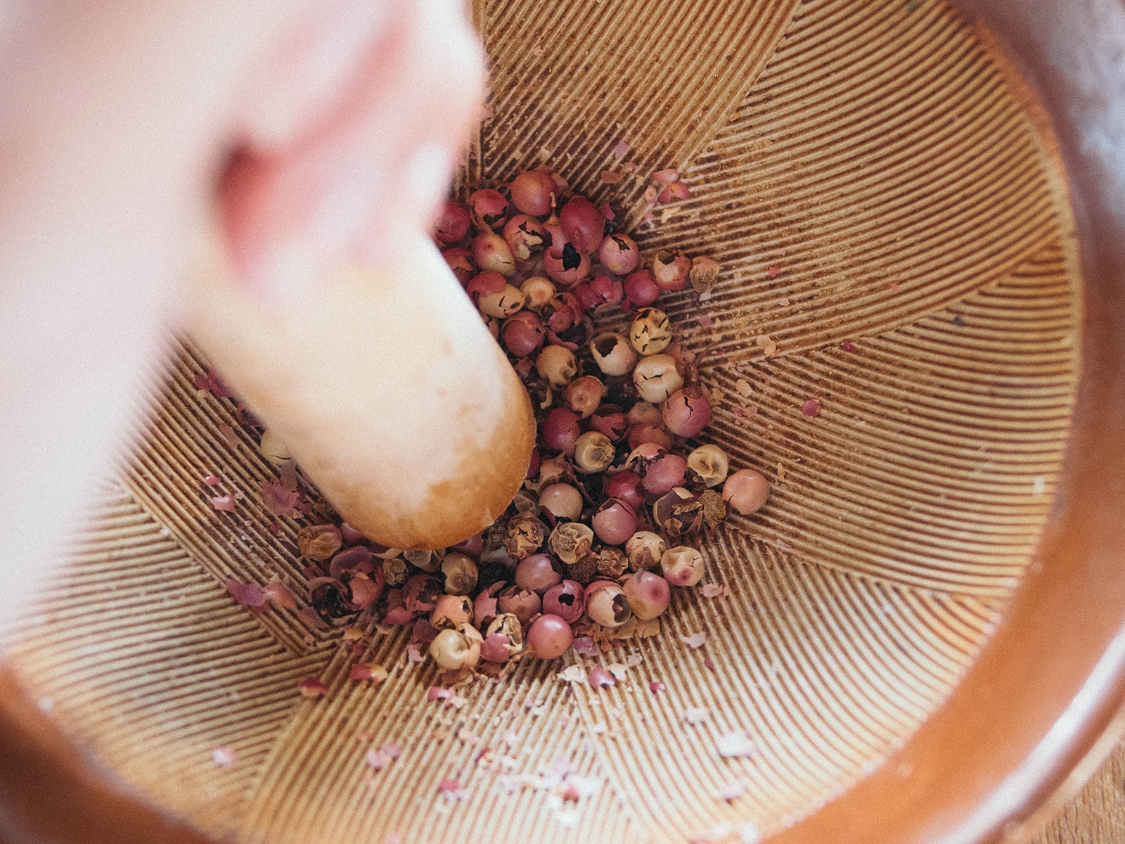 Pink peppercorns being crushed with a mortar and pestle