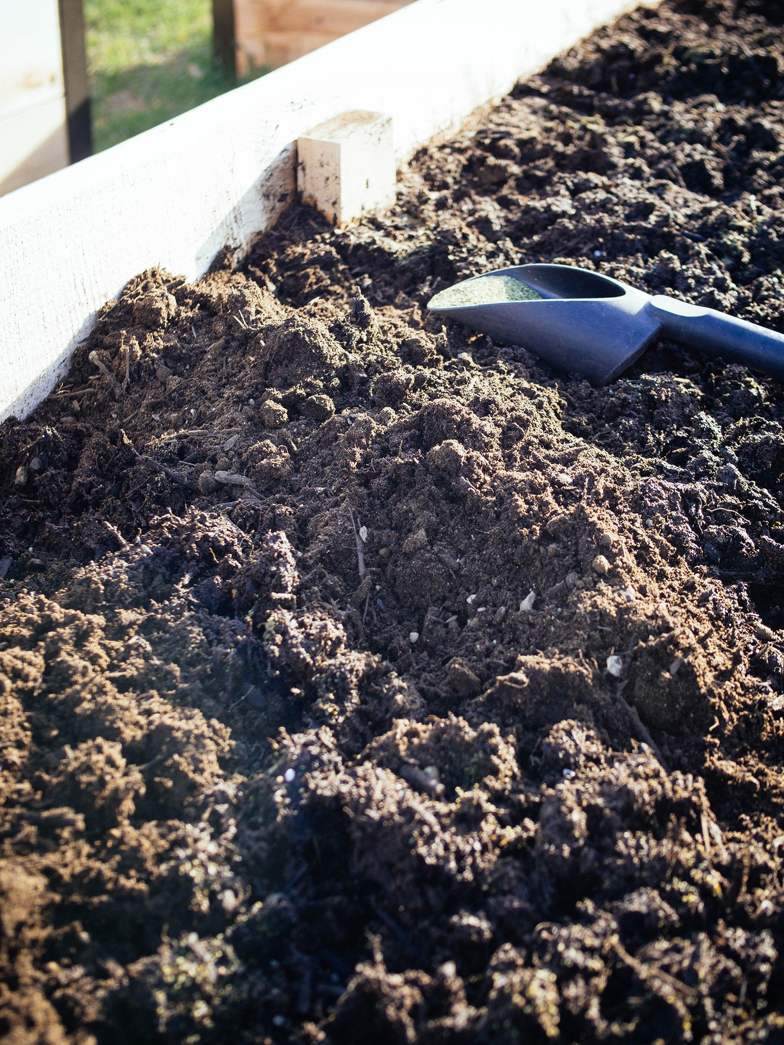Close-up of soil amended with fertilizer with a trowel in the background