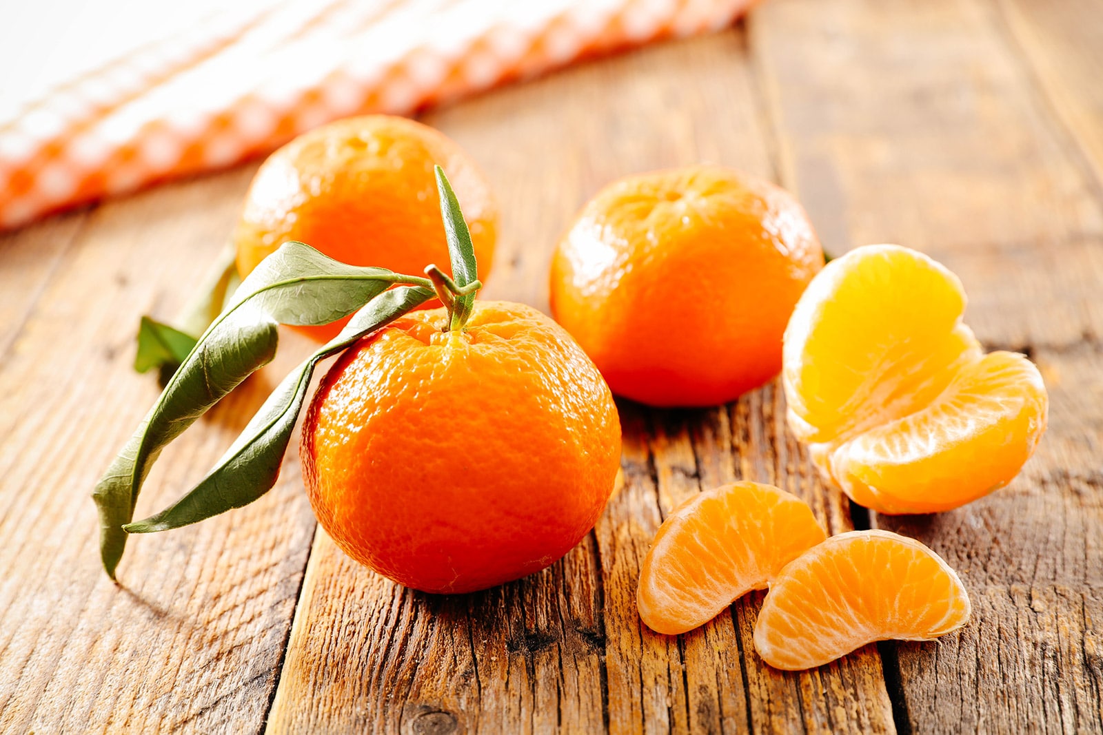 Whole clementines placed next to a peeled and separated clementine on a wooden surface