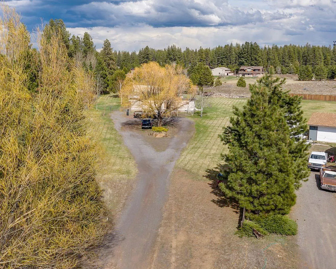 Real estate listing photo showing a rural property with pastures and mature trees