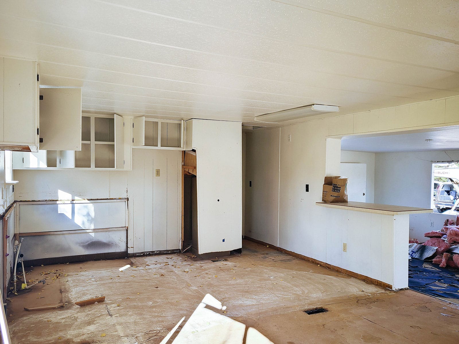 A gutted kitchen with no floors, white walls, and partially torn out cabinets