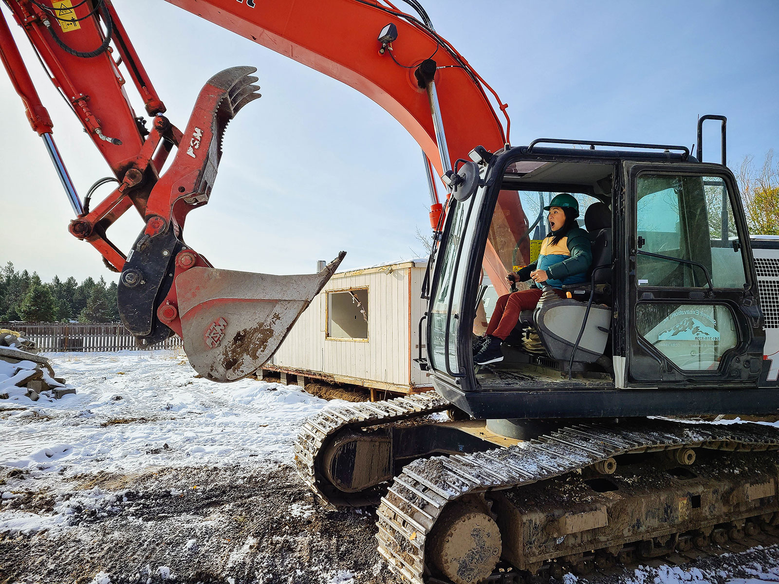 Woman in green hard hat pretending to drive a large excavator