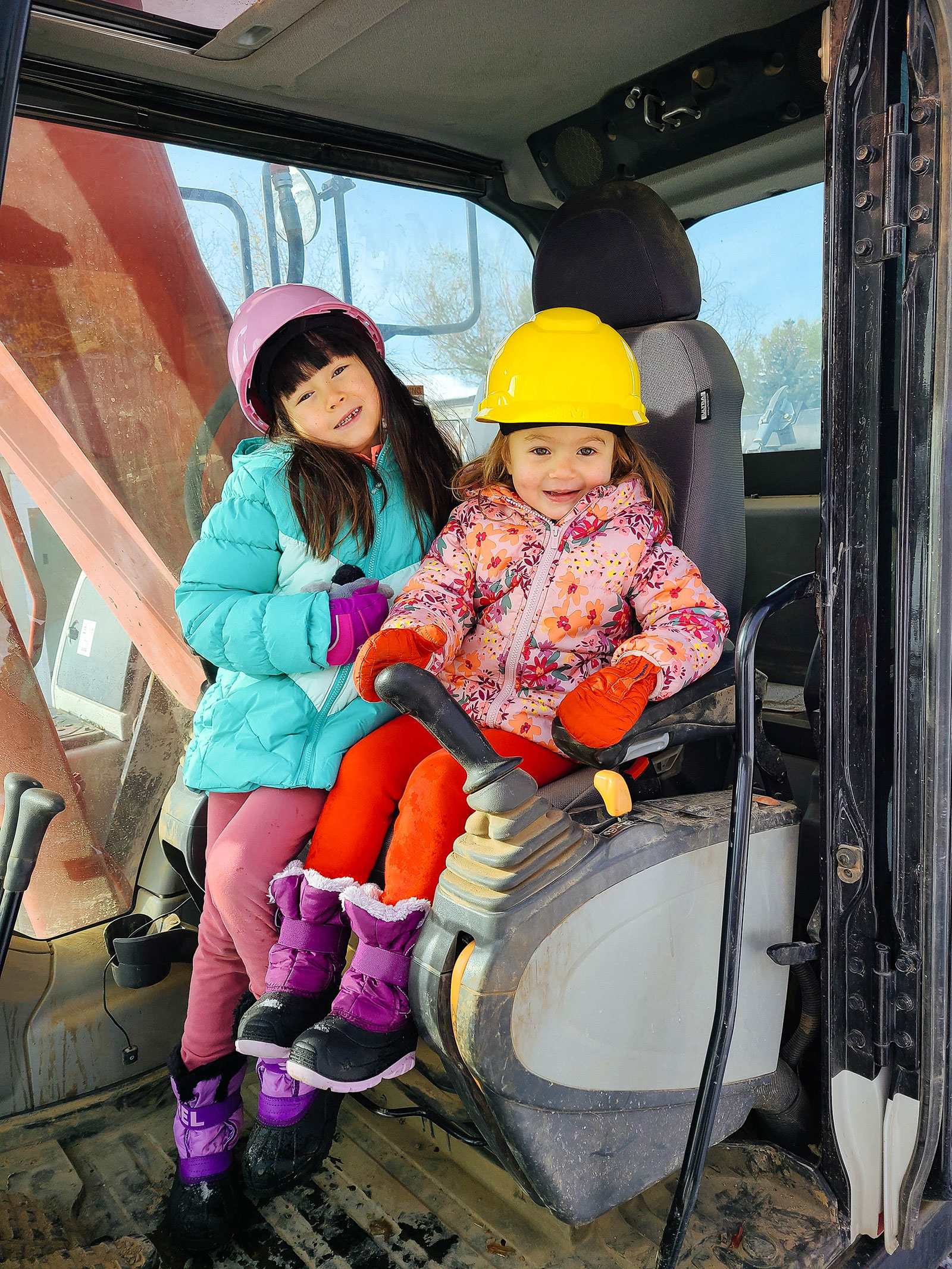Two young girls sitting in the driver's seat of an excavator