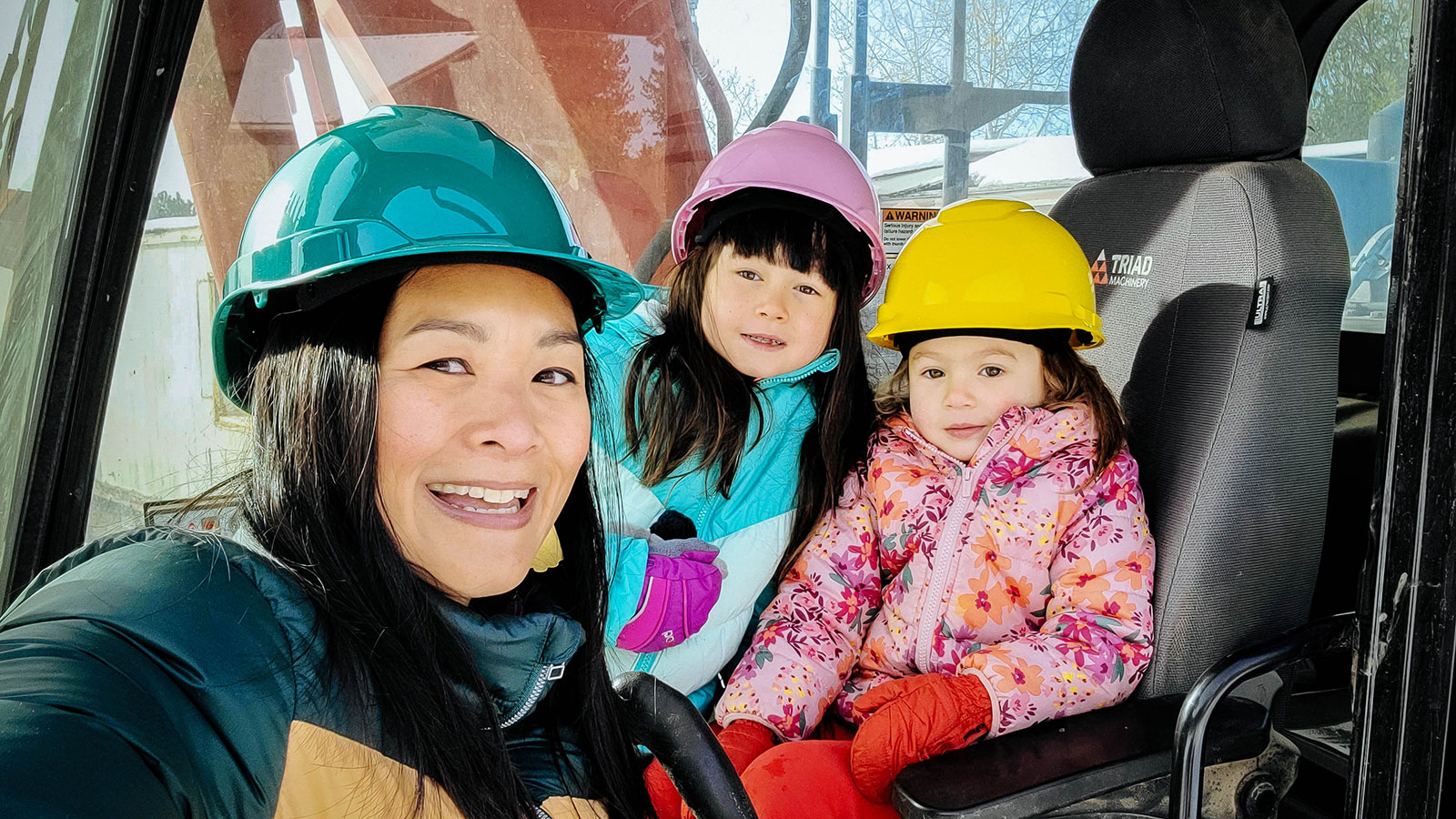 Mom and two daughters posing in the driver's seat of an excavator