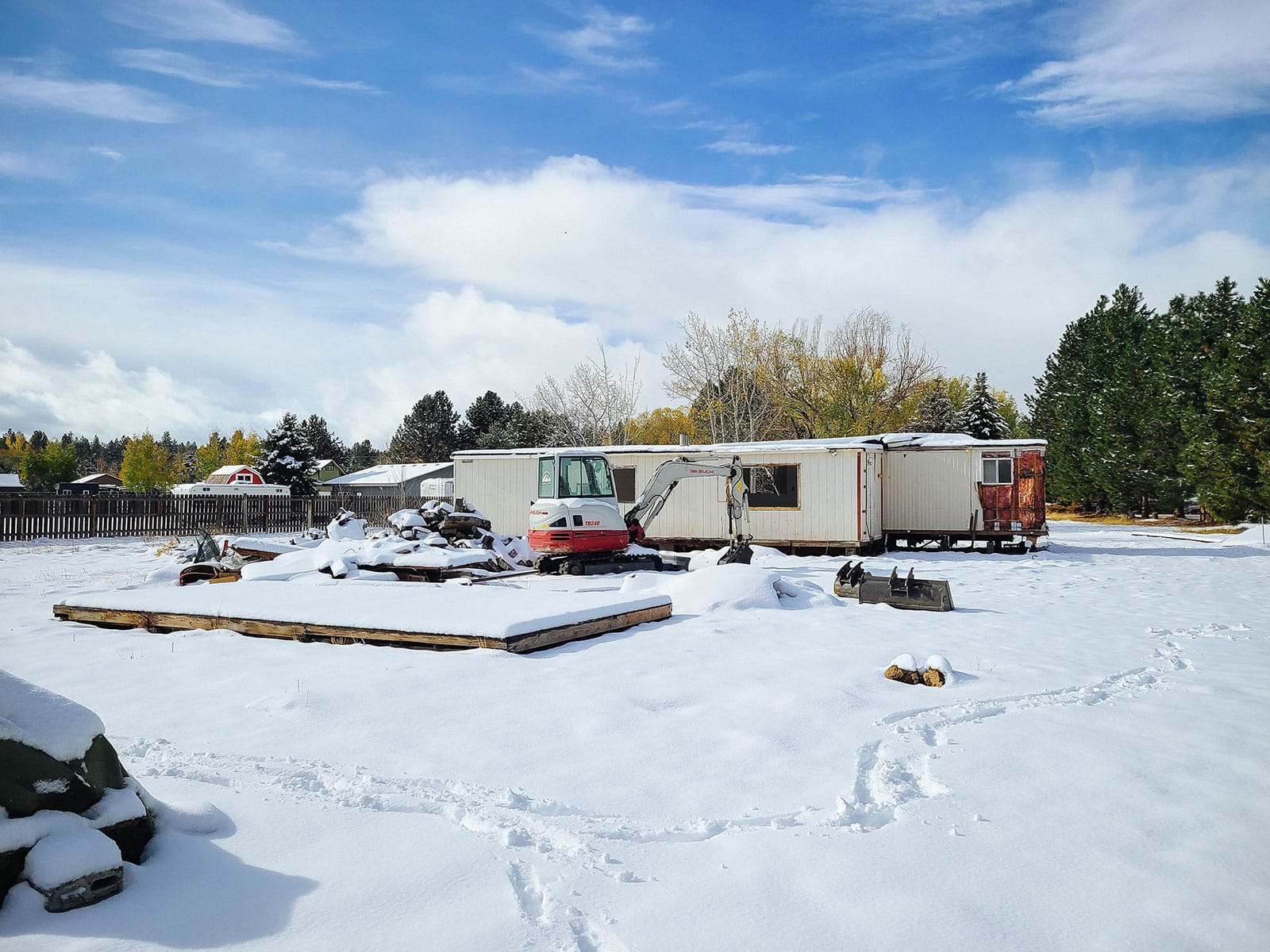 Fresh snow blanketing a yard with an older manufactured home and mini excavator in front of it