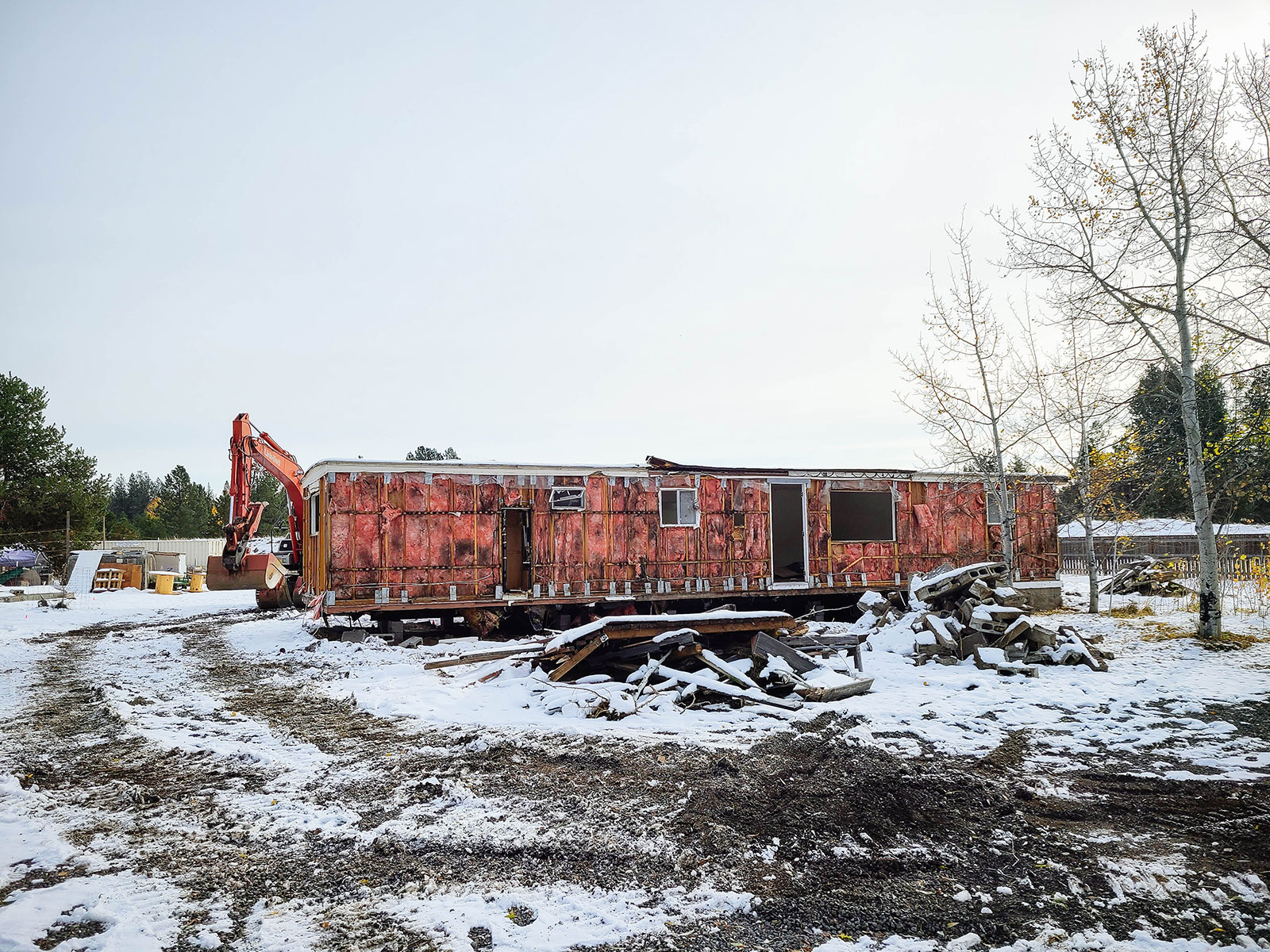 A manufactured home with all the siding removed during excavation, revealing pink insulation