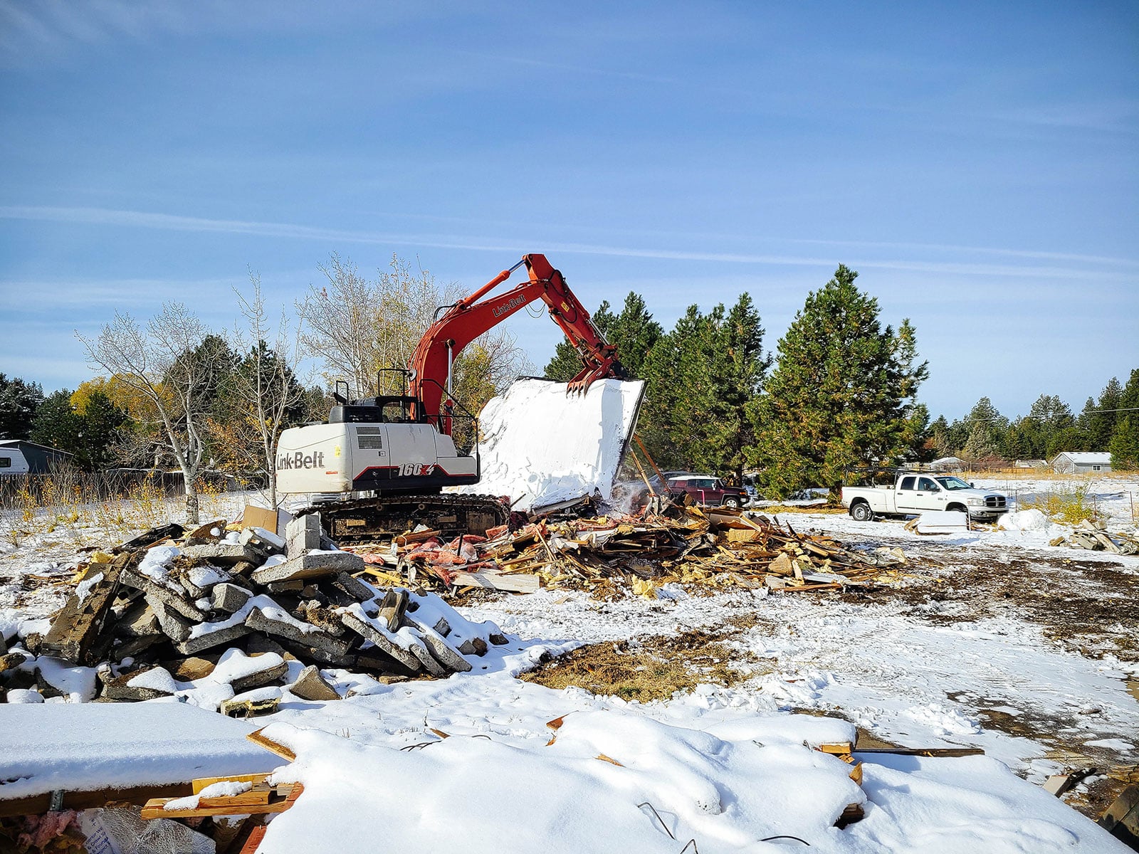An excavator moving a large wall that was demolished from a home