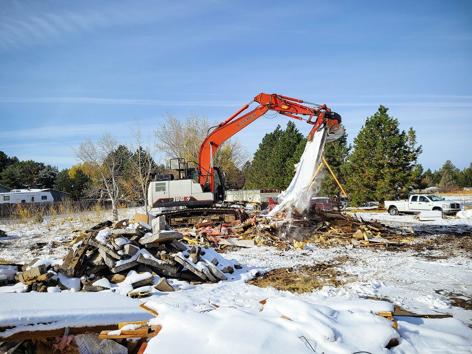 A large excavator moving part of a large wall that was demolished from a home