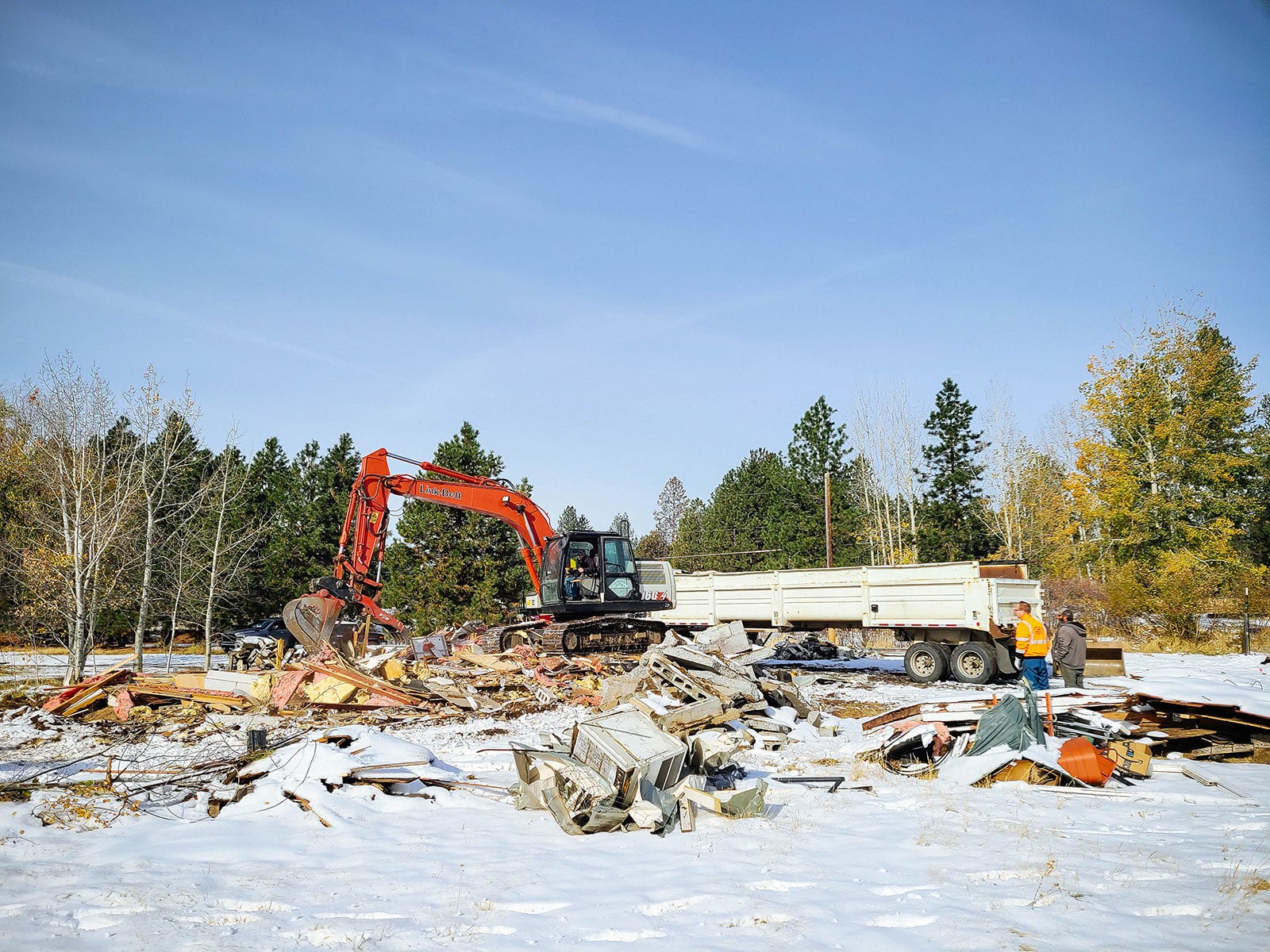 Excavator moving piles of debris into a large dump truck