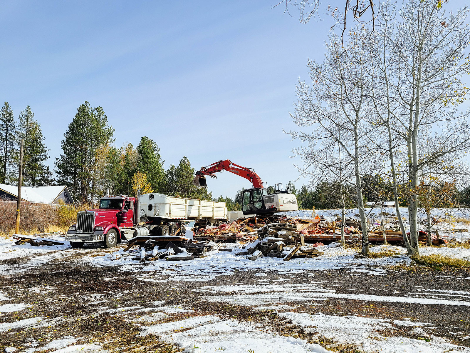 Excavator moving piles of debris into a large dump truck at a residential demo site