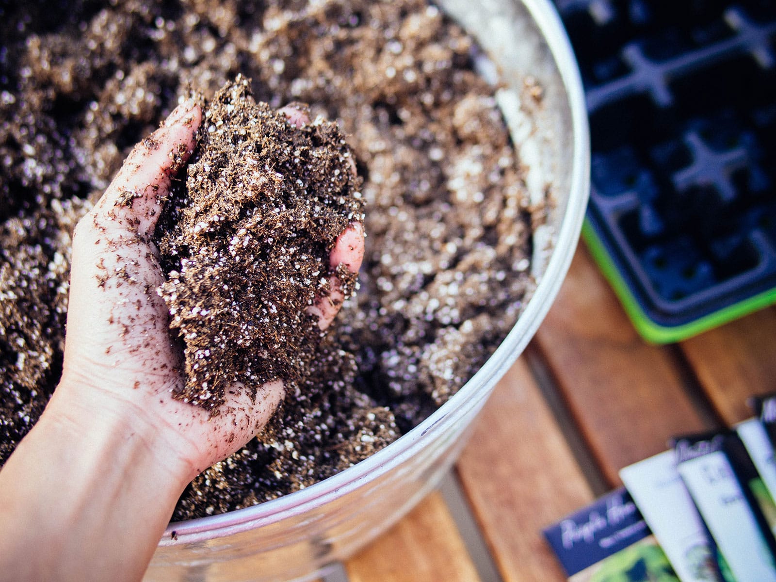Close-up of hand grabbing a fistful of potting soil from a galvanized tub