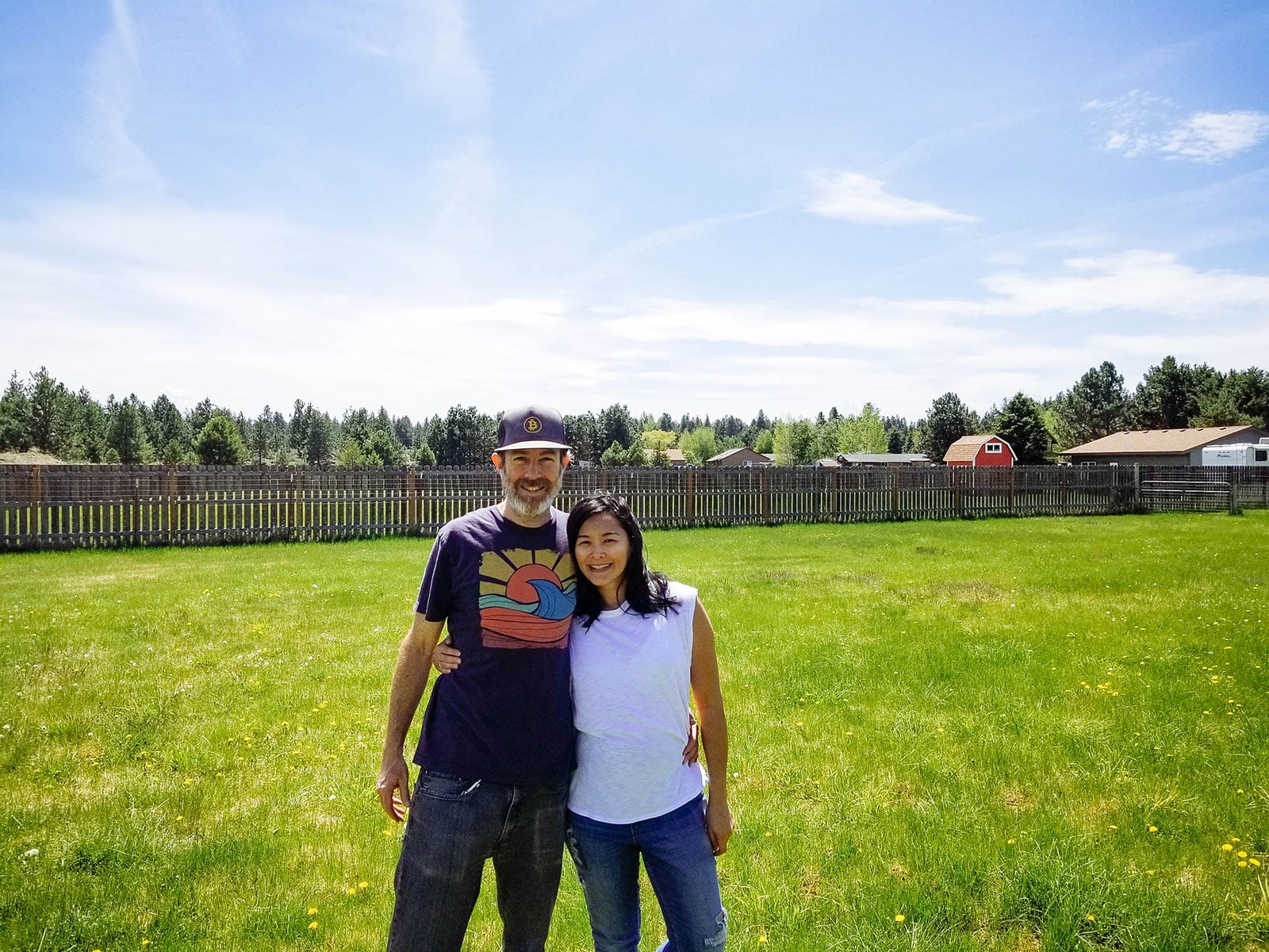 Smiling man and woman standing on an empty grassy parcel with a wooden fence in the background