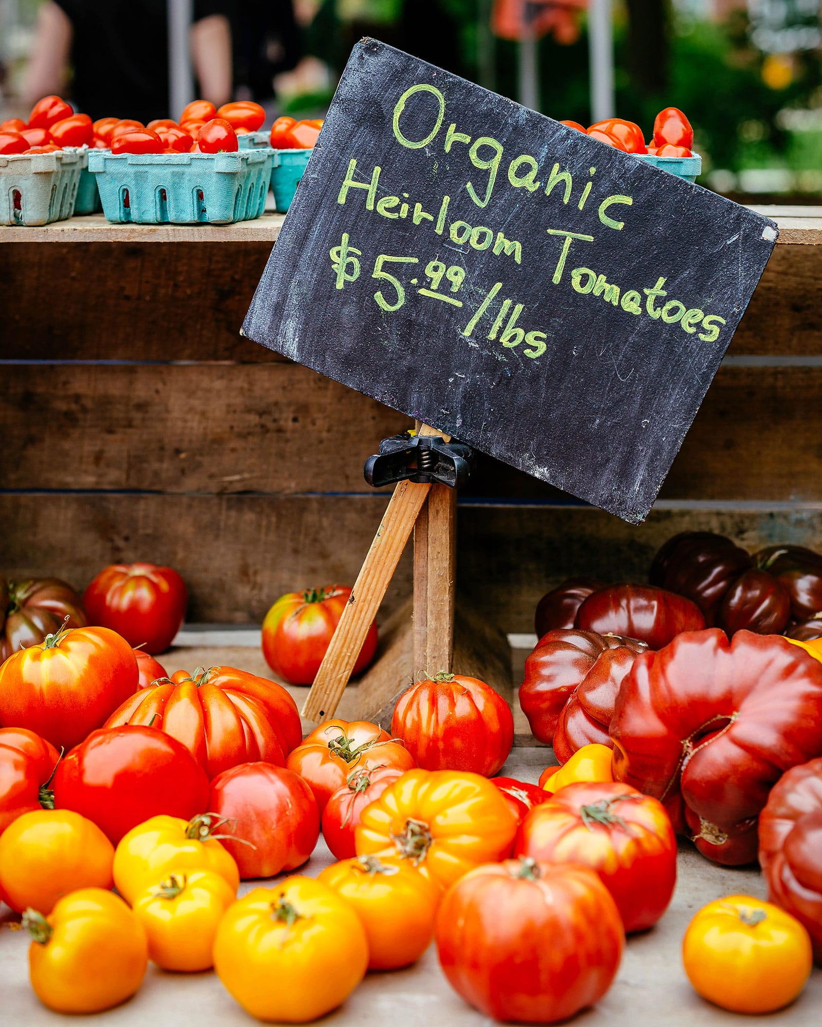 Heirloom tomatoes on display at a farmers' market stall with a chalkboard sign showing the price