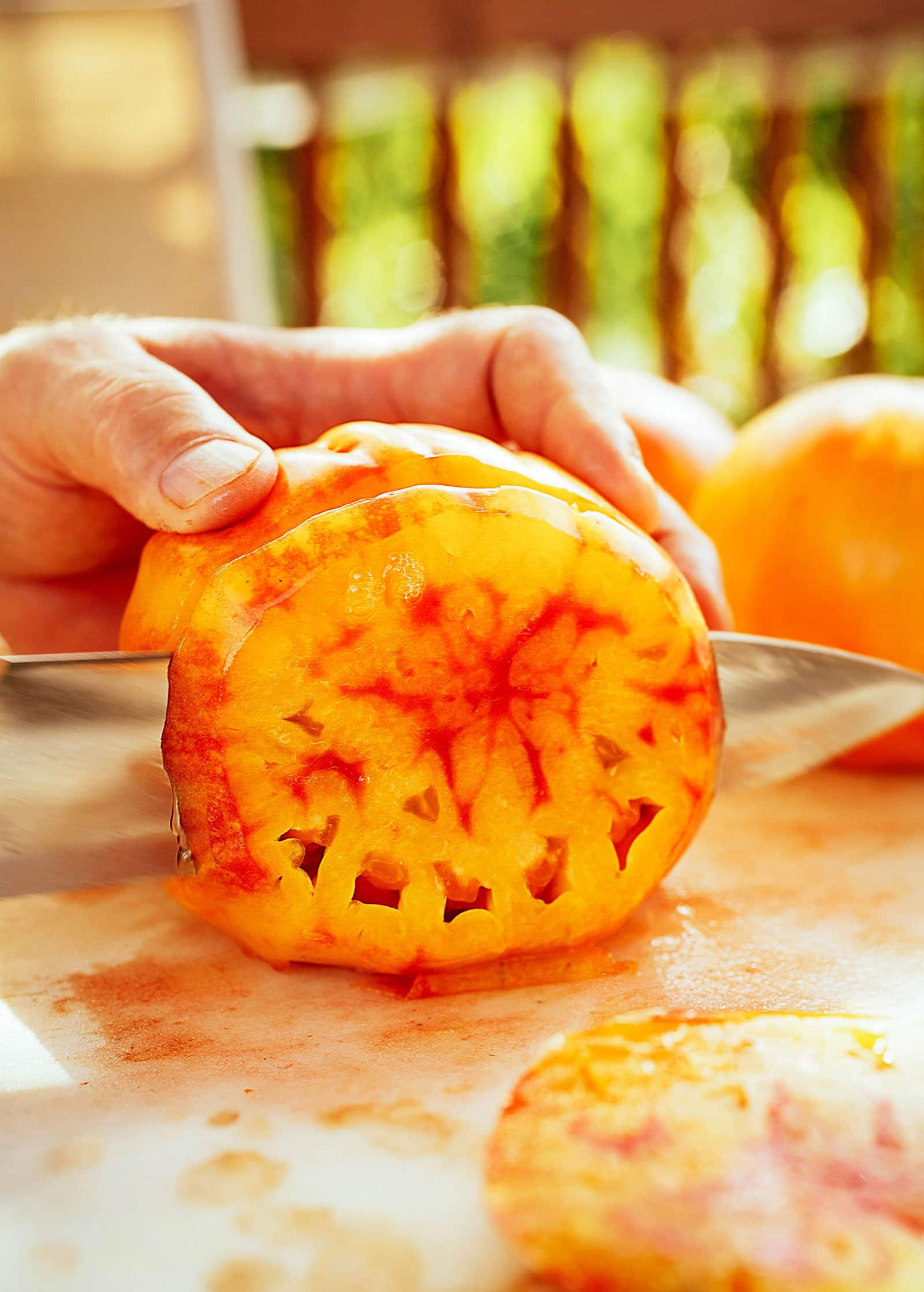 Knife slicing into a big juicy orange and red heirloom tomato on a cutting board
