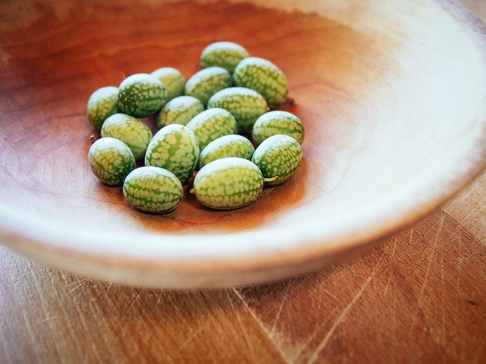 A handful of cucamelons (Mexican sour gherkins) in a shallow wooden bowl on a wooden surface