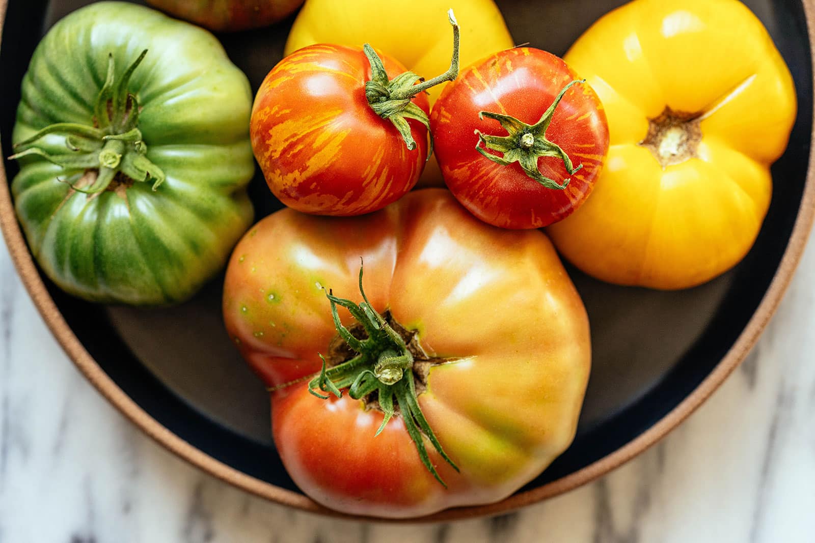 Colorful group of heirloom tomatoes ripening in a bowl on a marble counter
