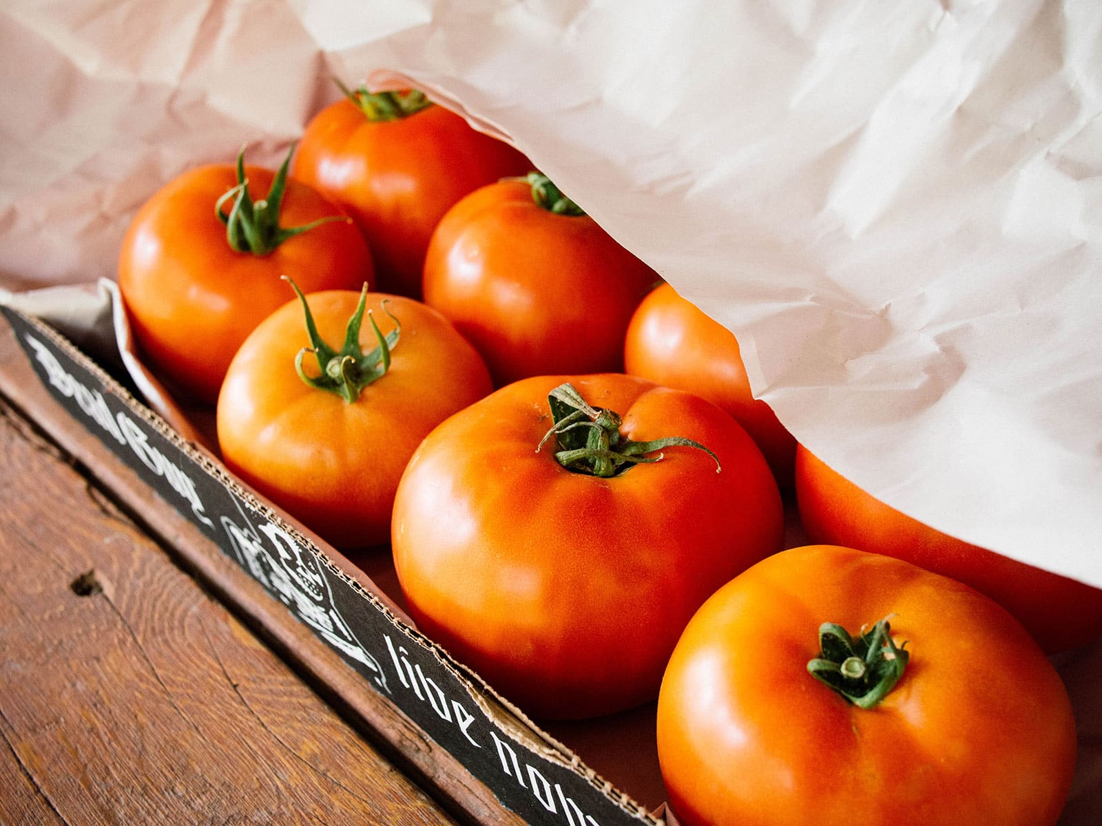 Beefsteak tomatoes ripening in a cardboard tray under sheets of newsprint