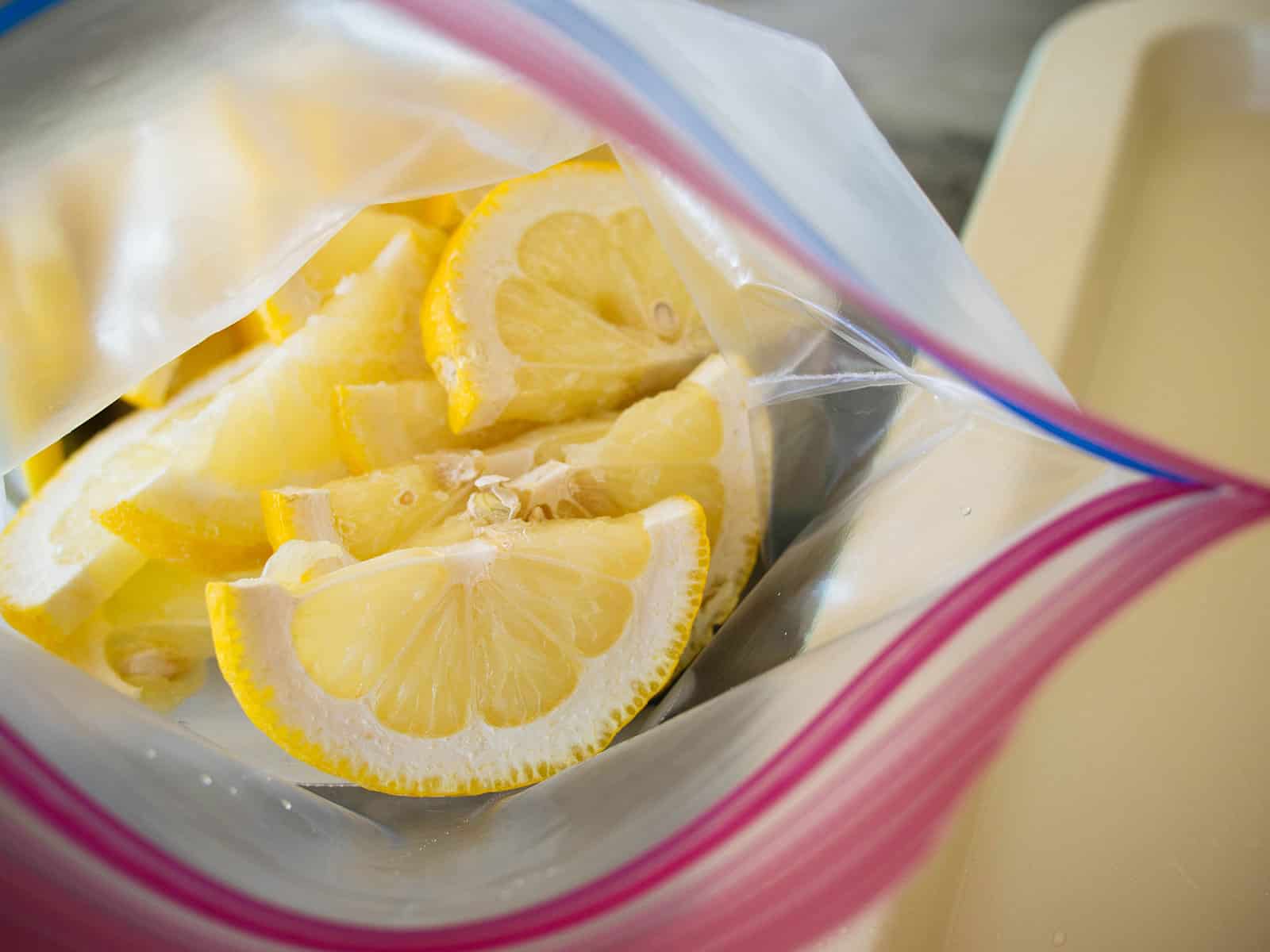 Frozen half slices of lemons in a plastic zip-top bag next to a cream-colored baking sheet
