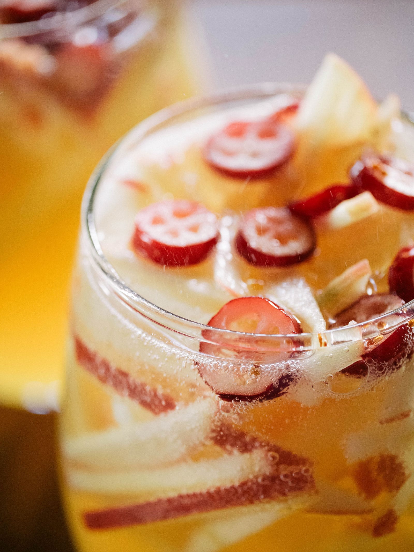 Close-up of sliced cranberries, sliced apples, and fizzing bubbles in a glass of sparkling apple cider sangria
