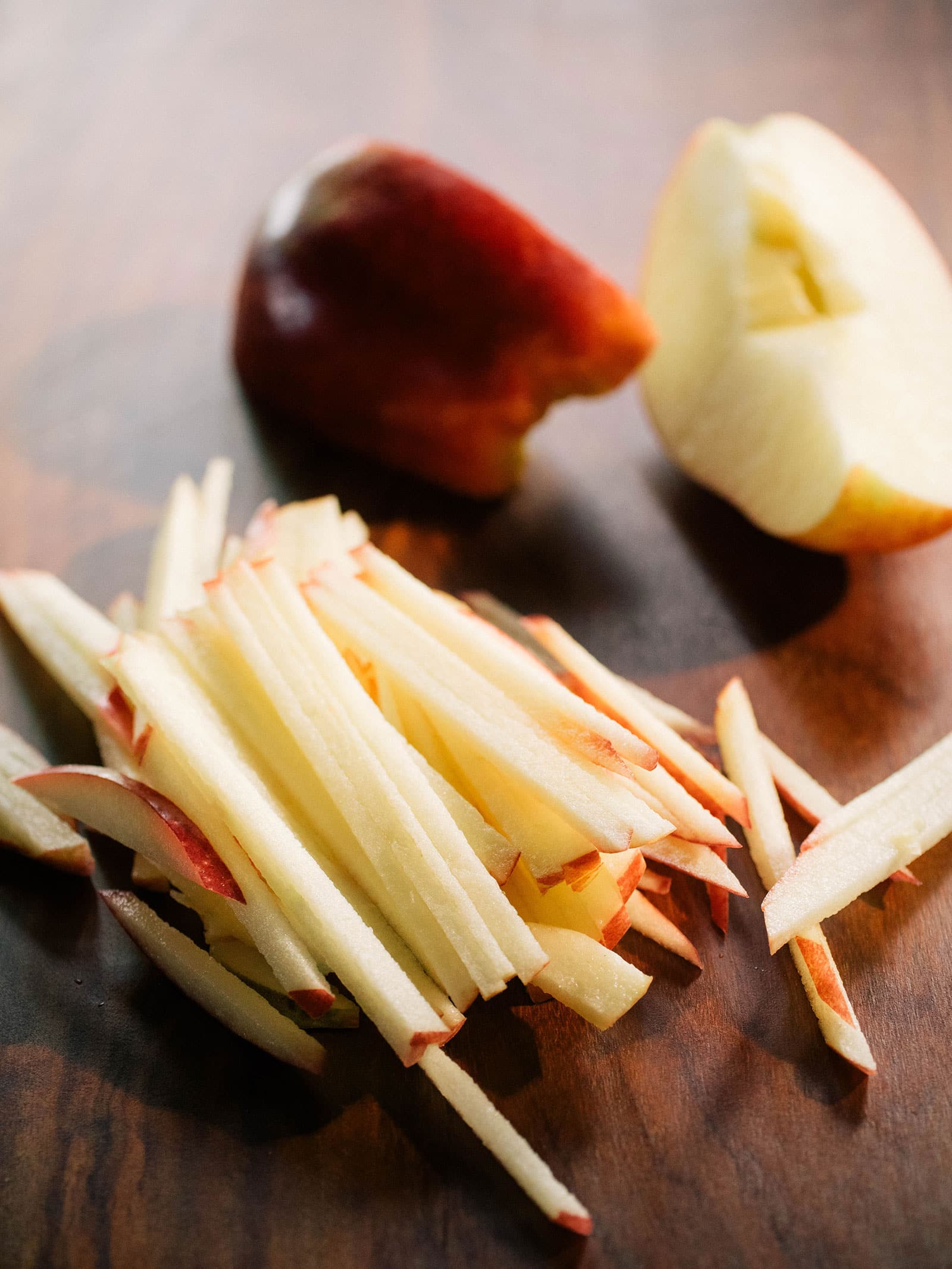 Red apple cut into matchsticks on a wooden cutting board
