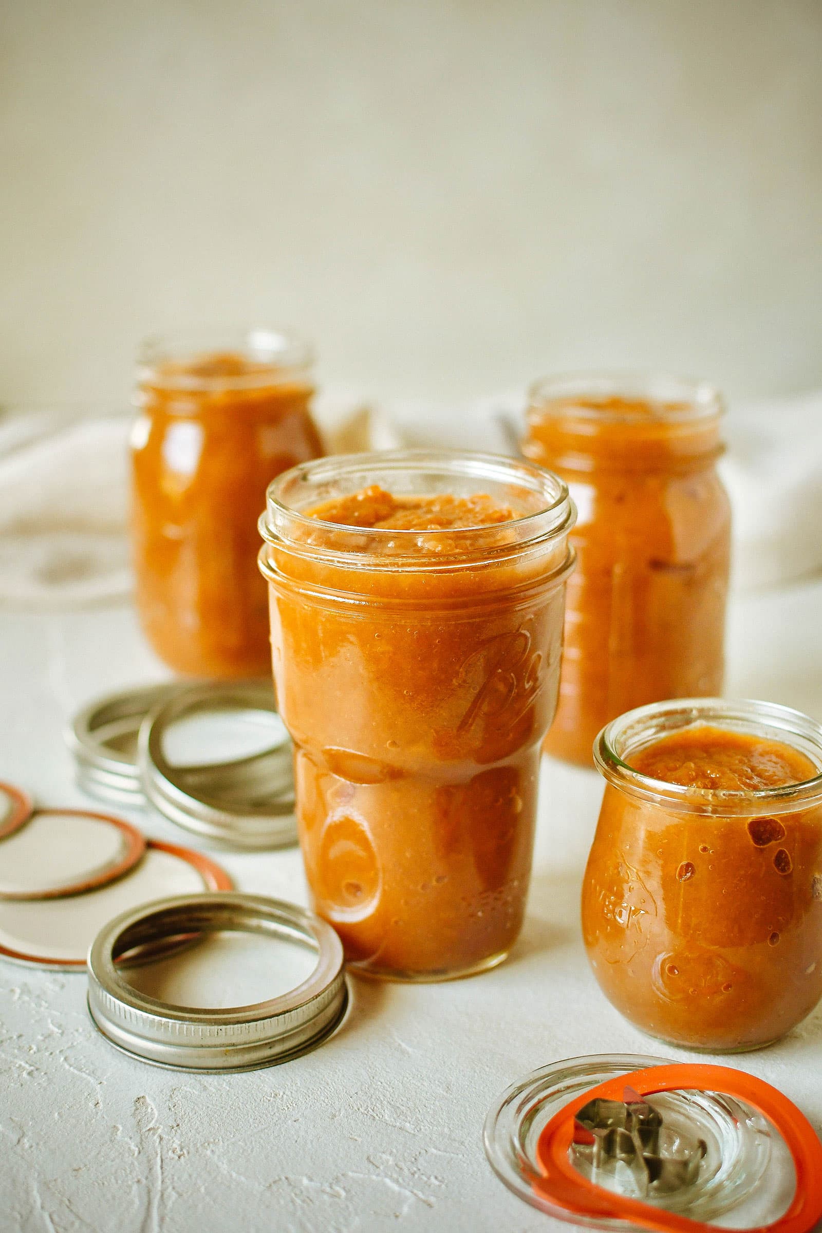 Various pint and half-pint jars of spiced apple-pear butter on a white table, with lids and rings arranged around them