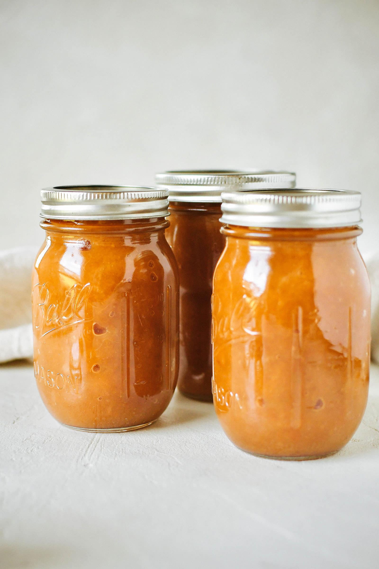 Three pint jars of processed apple-pear butter on a white table