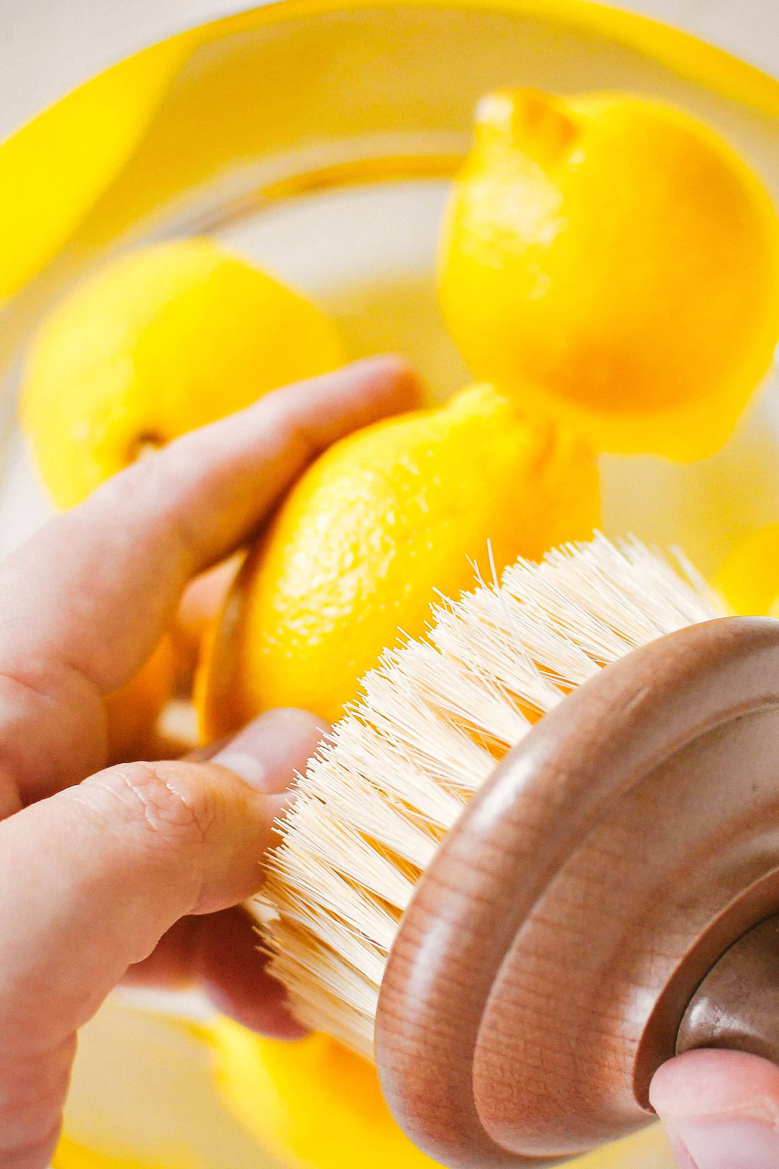Hand scrubbing a lemon with a wooden natural bristle brush