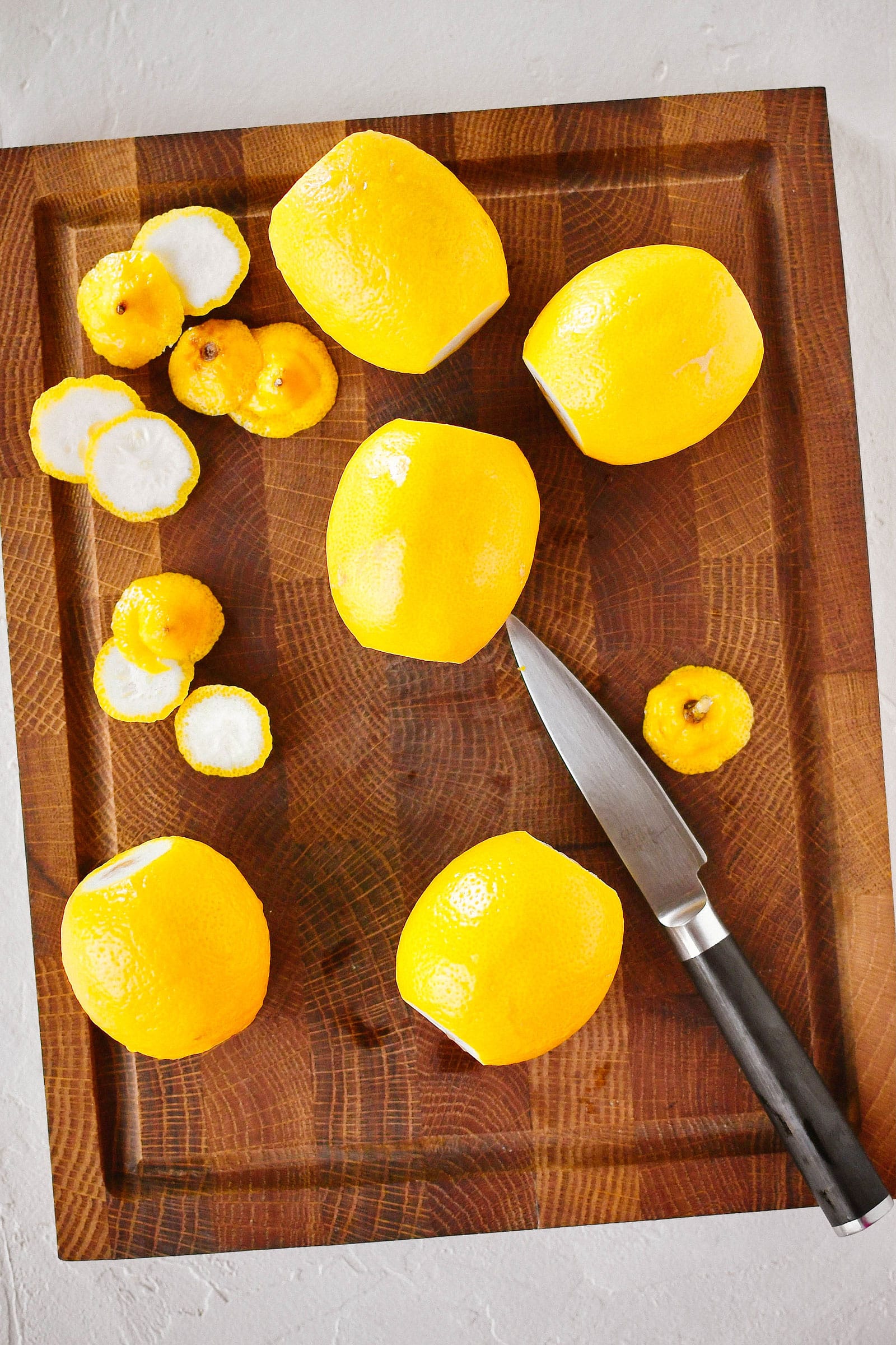 Lemons and a knife on a wooden cutting board, with the ends cut off on each lemon