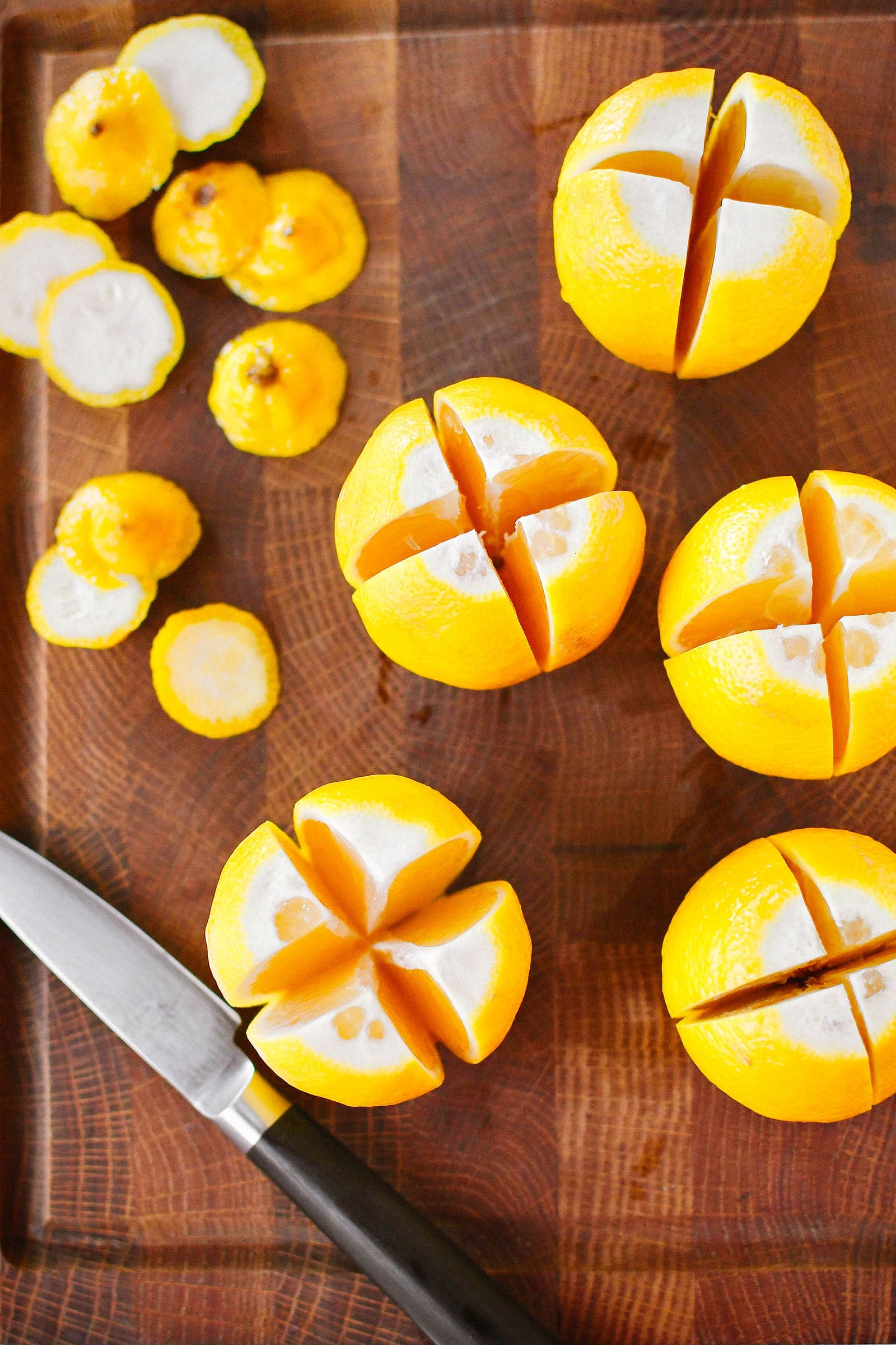 Lemons and a knife on a cutting board, with each lemon quartered lengthwise