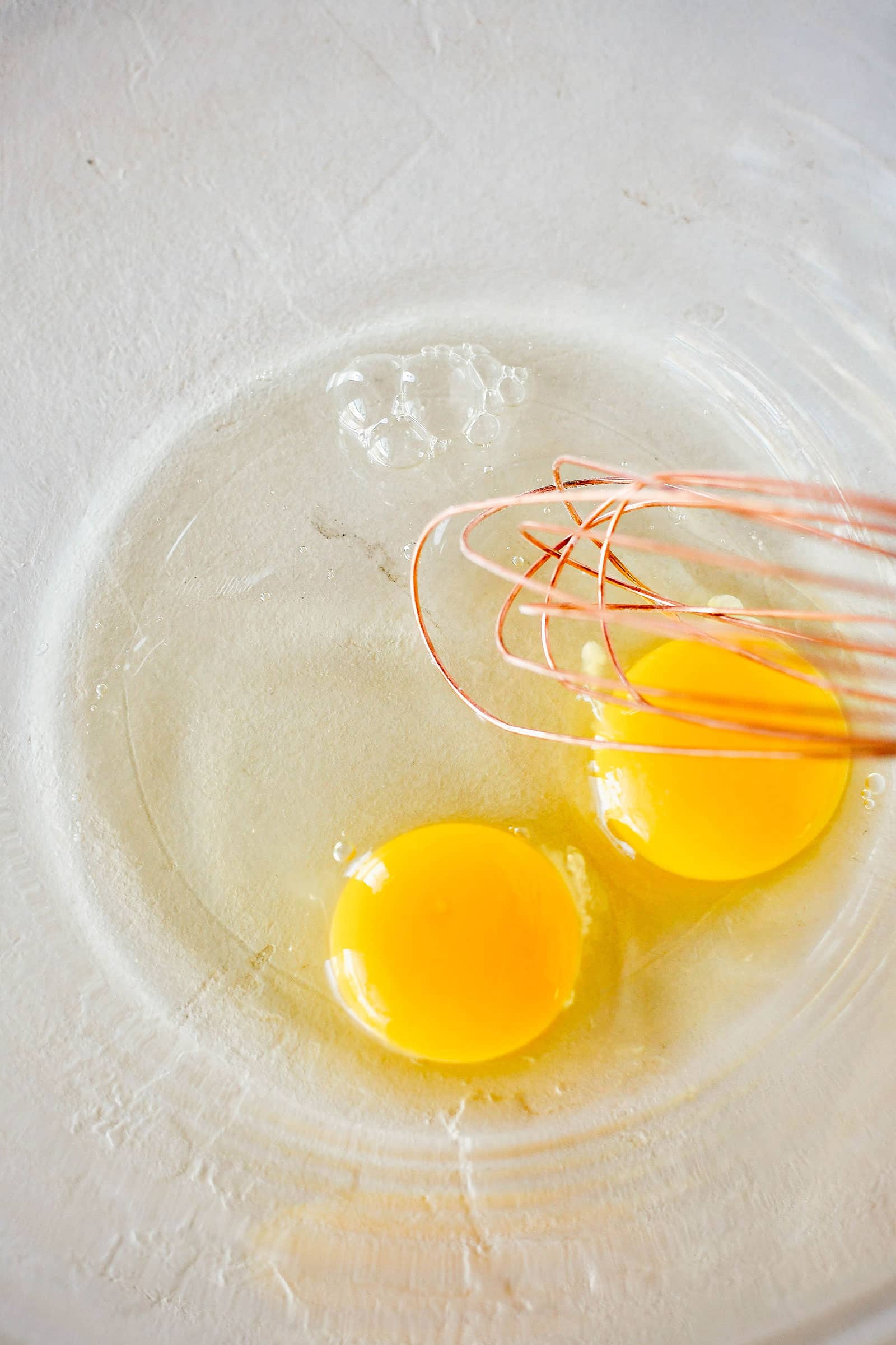 Two eggs cracked into a bowl with a whisk about to mix them