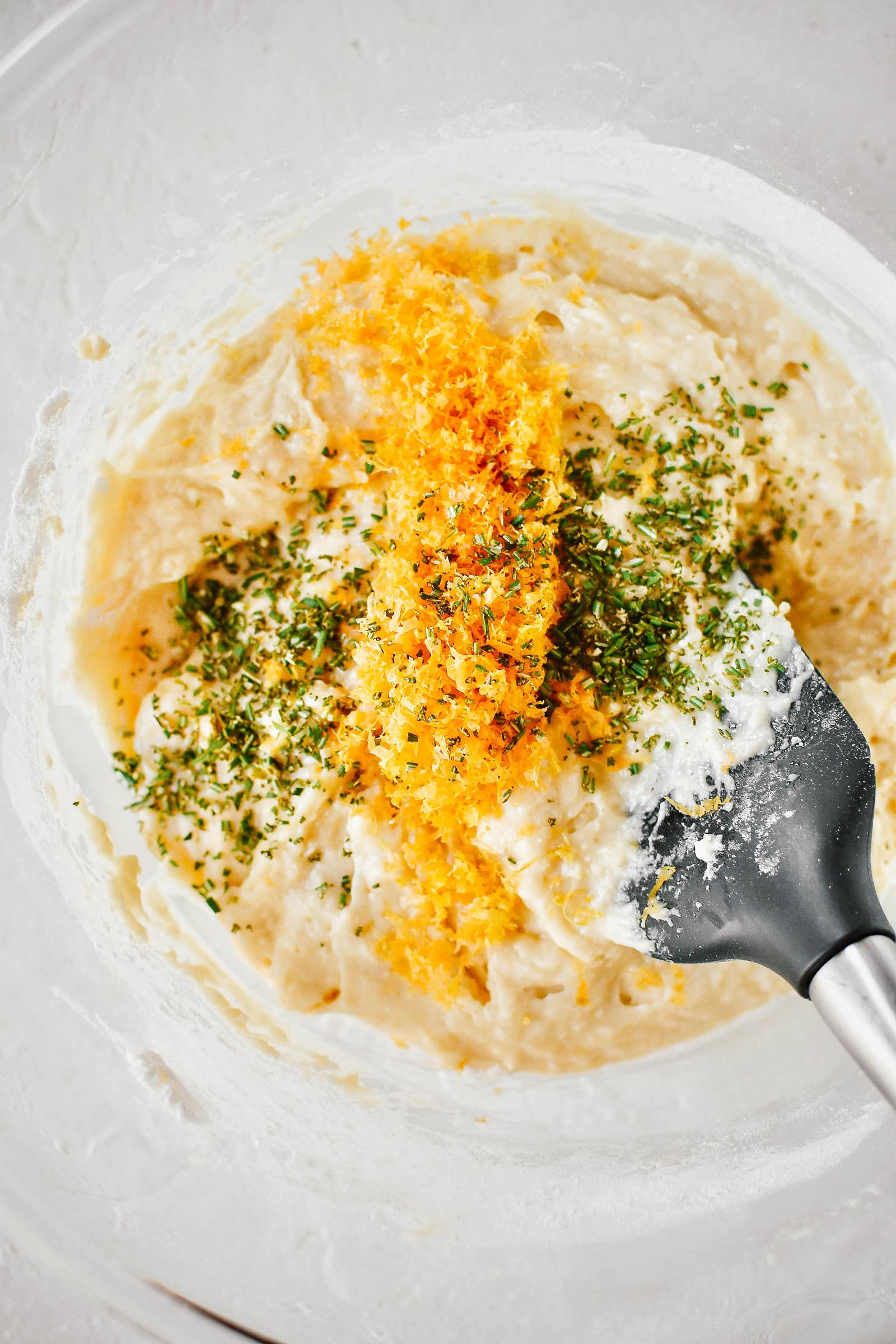 A spoon mixing grapefruit zest and rosemary into a bowl of bread batter