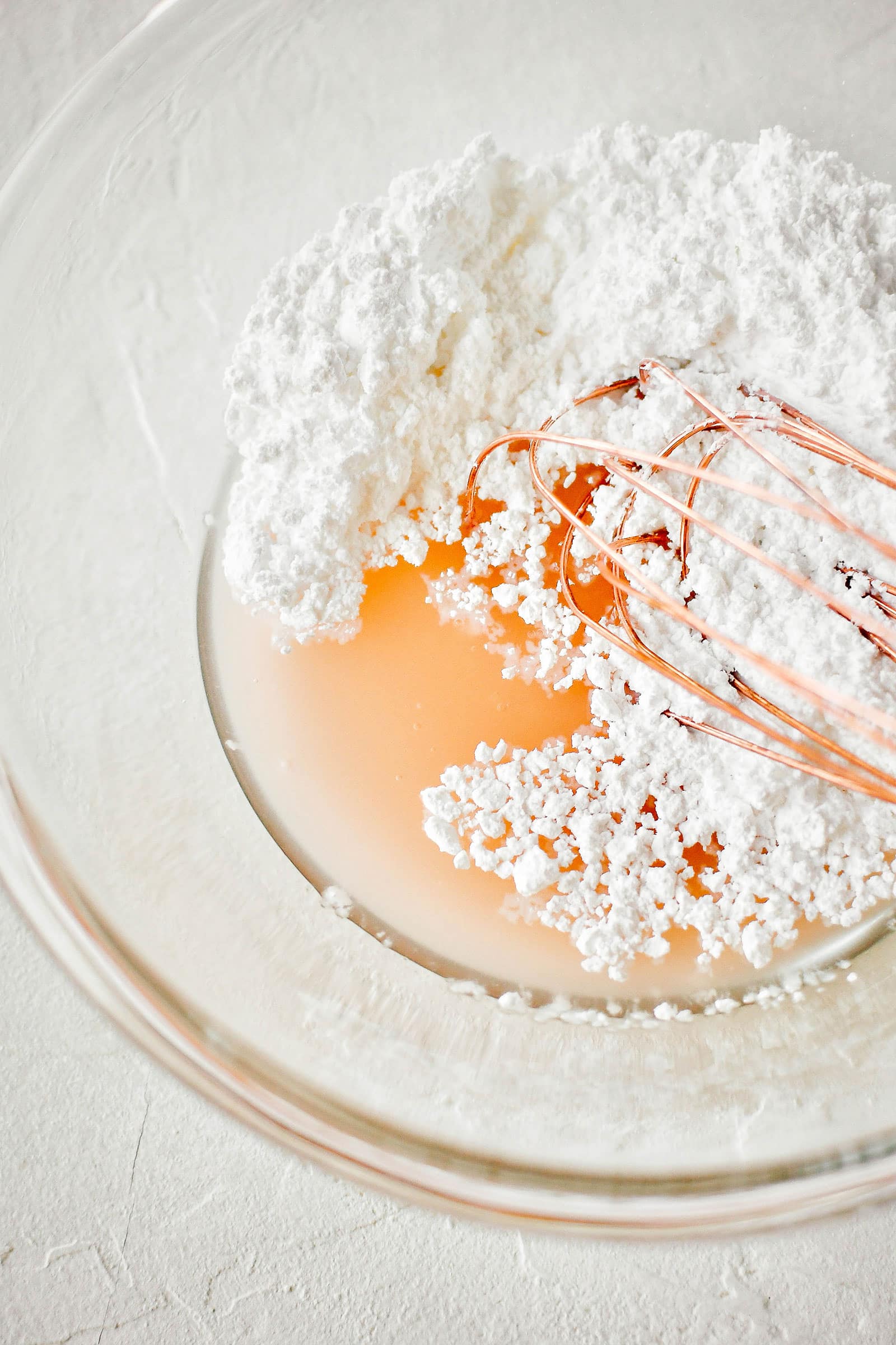 Close-up of whisk mixing powdered sugar into a bowl of grapefruit juice