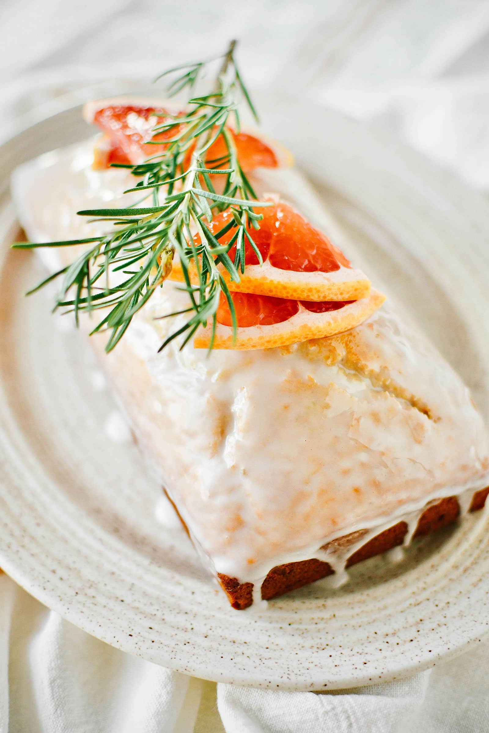 A glazed loaf of grapefruit-rosemary bread garnished with grapefruit slices and a rosemary sprig on top