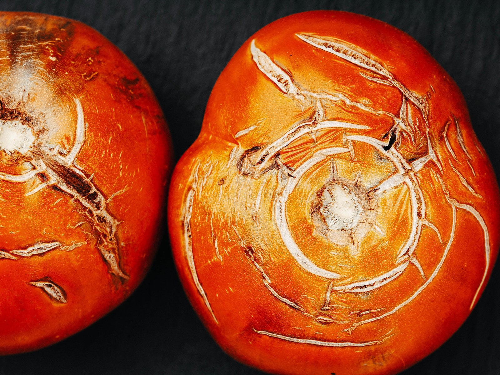 Overhead shot of red tomatoes on a dark surface, with concentric cracks on the stem side of the fruit