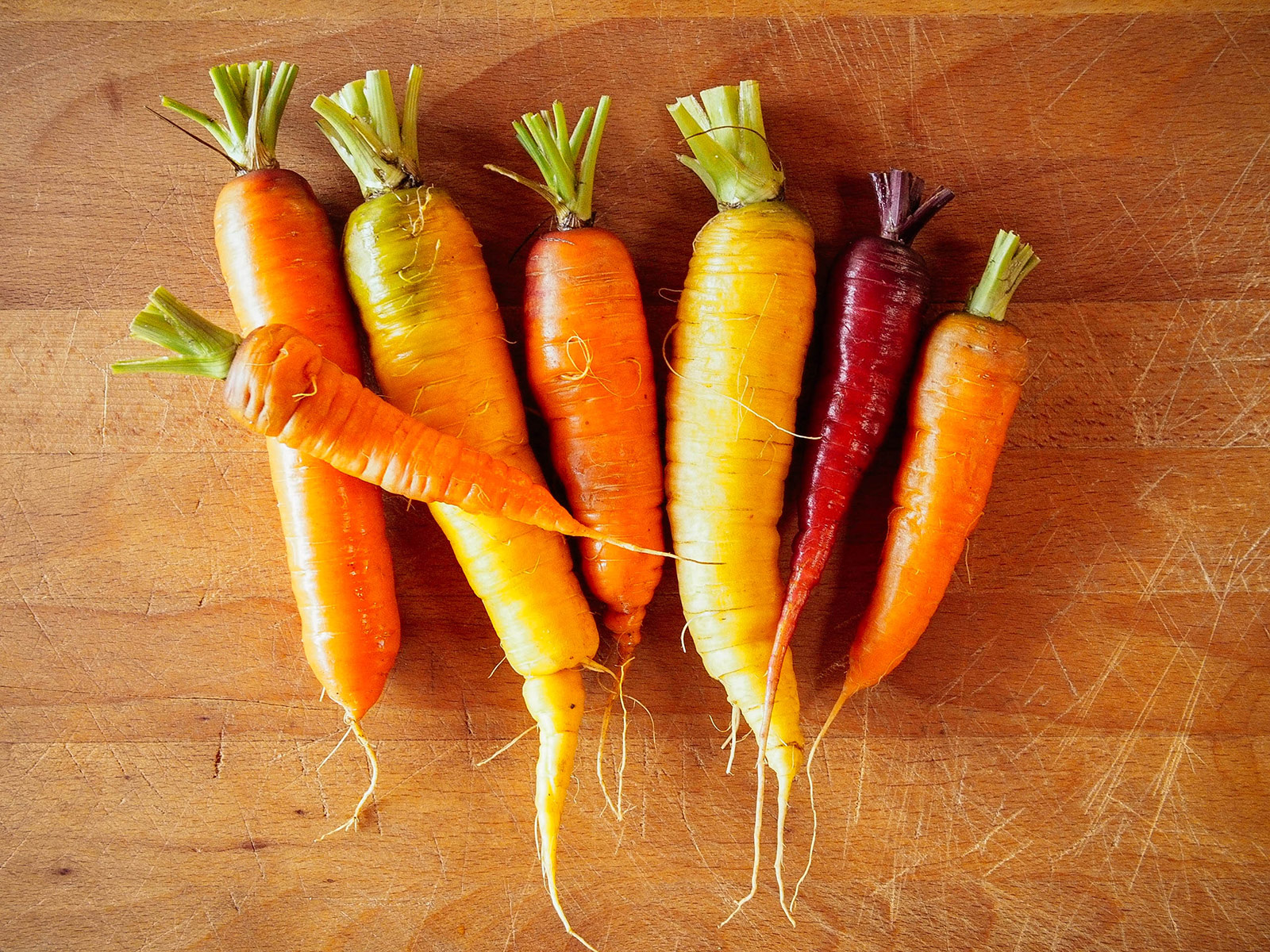 Seven colorful yellow, orange, and purple carrots arranged on a butcher block surface