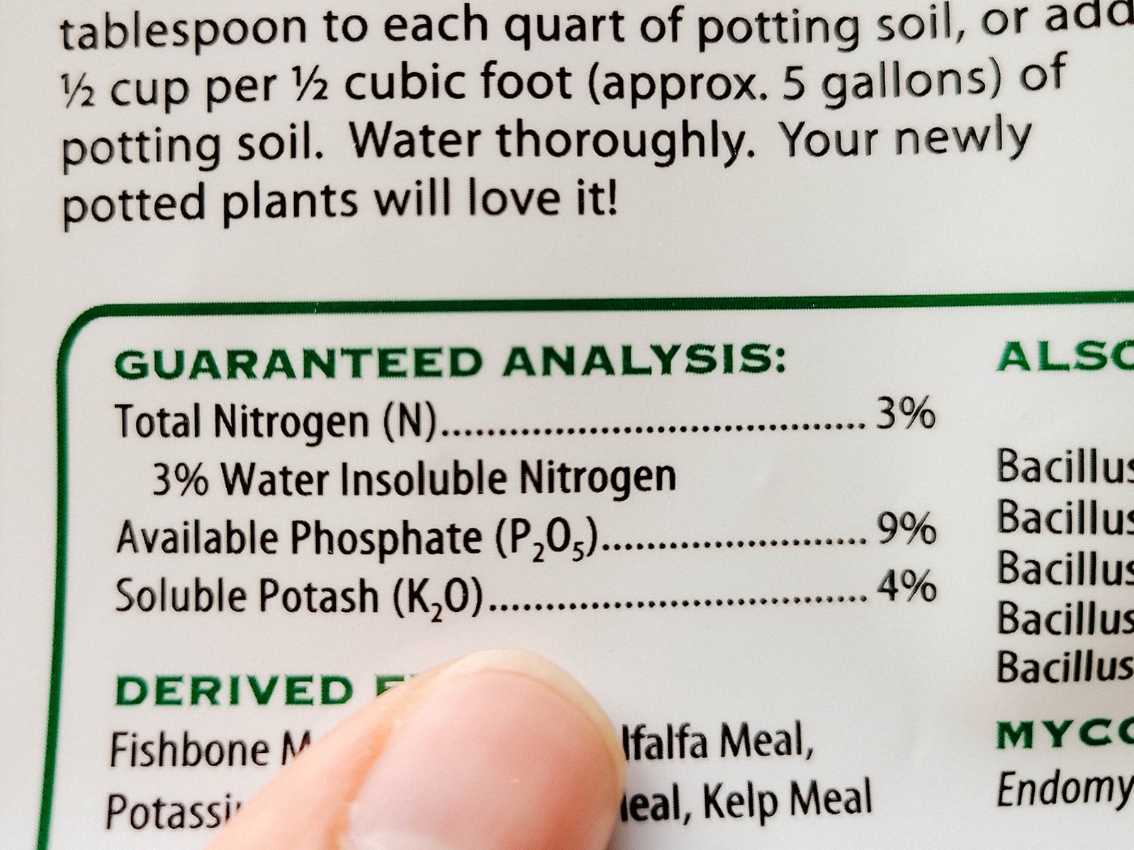 A finger pointing to a fertilizer label showing the guaranteed analysis in the fertilizer bag