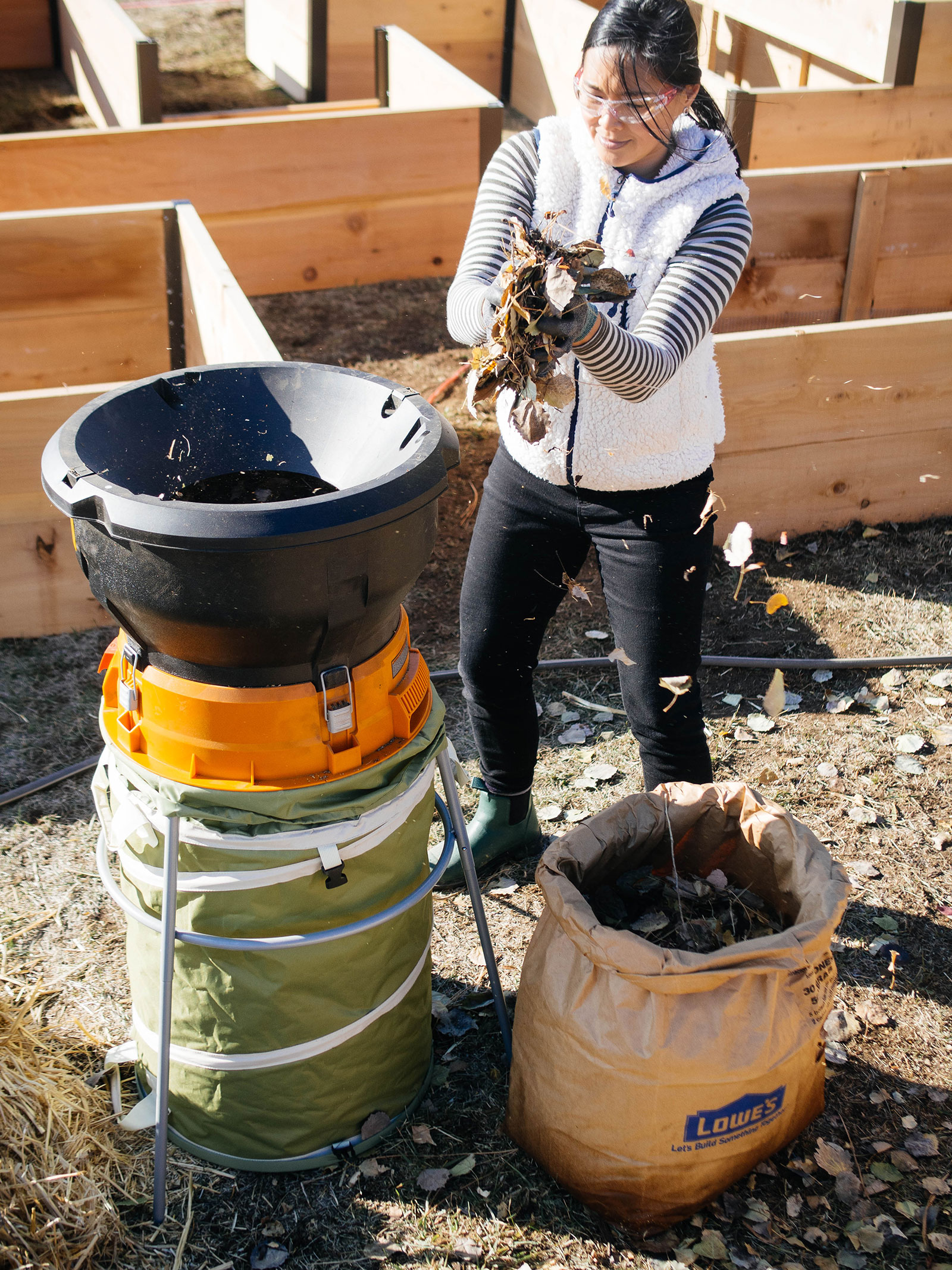 Linda Ly putting a handful of dried leaves into an electric leaf mulcher in a garden with several wooden raised beds in the background